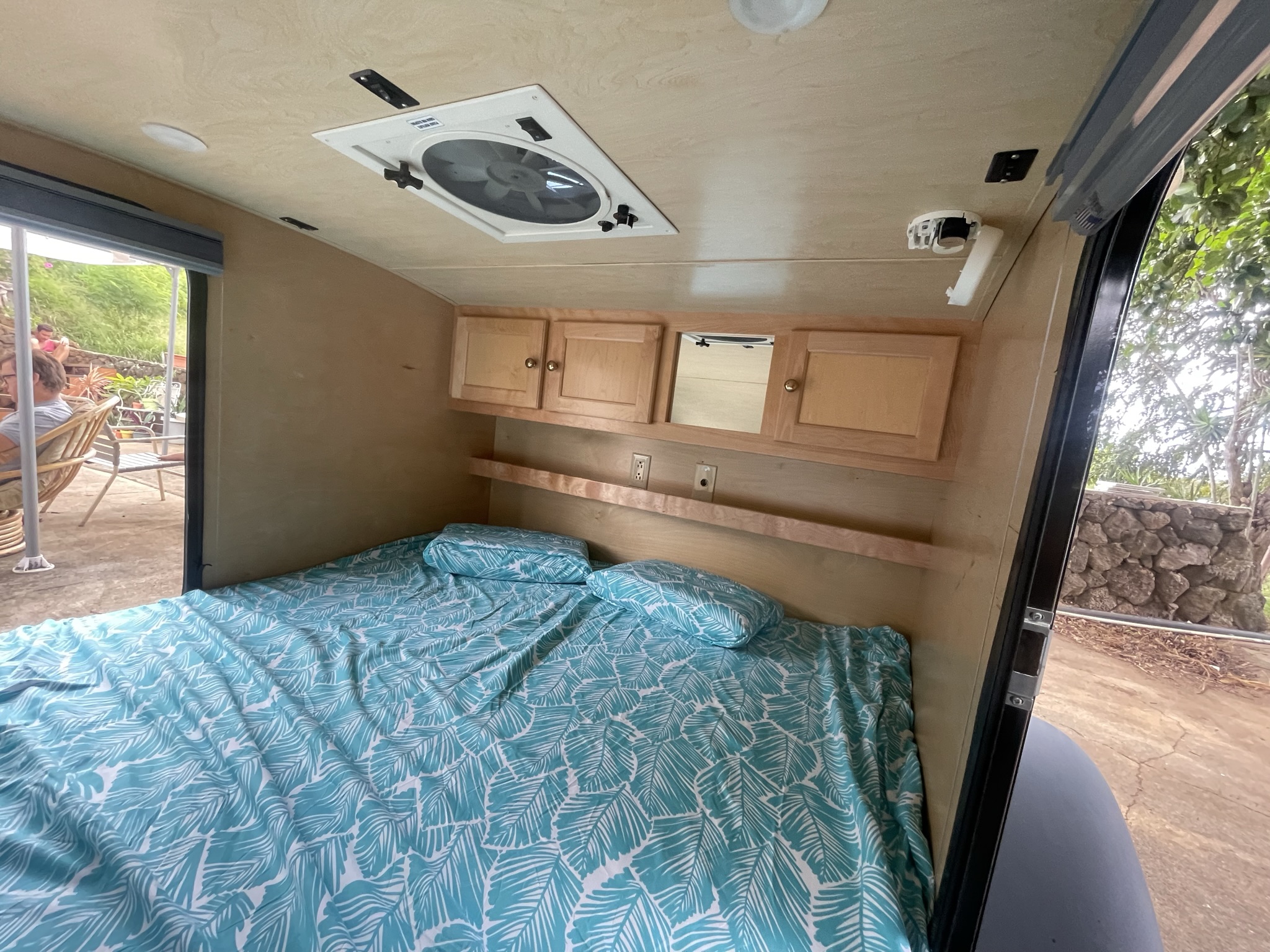 Cozy RV rental interior featuring a patterned bed, overhead storage, and ceiling fan. View of outdoor patio area.. Little Guy Silver Shadow 2015