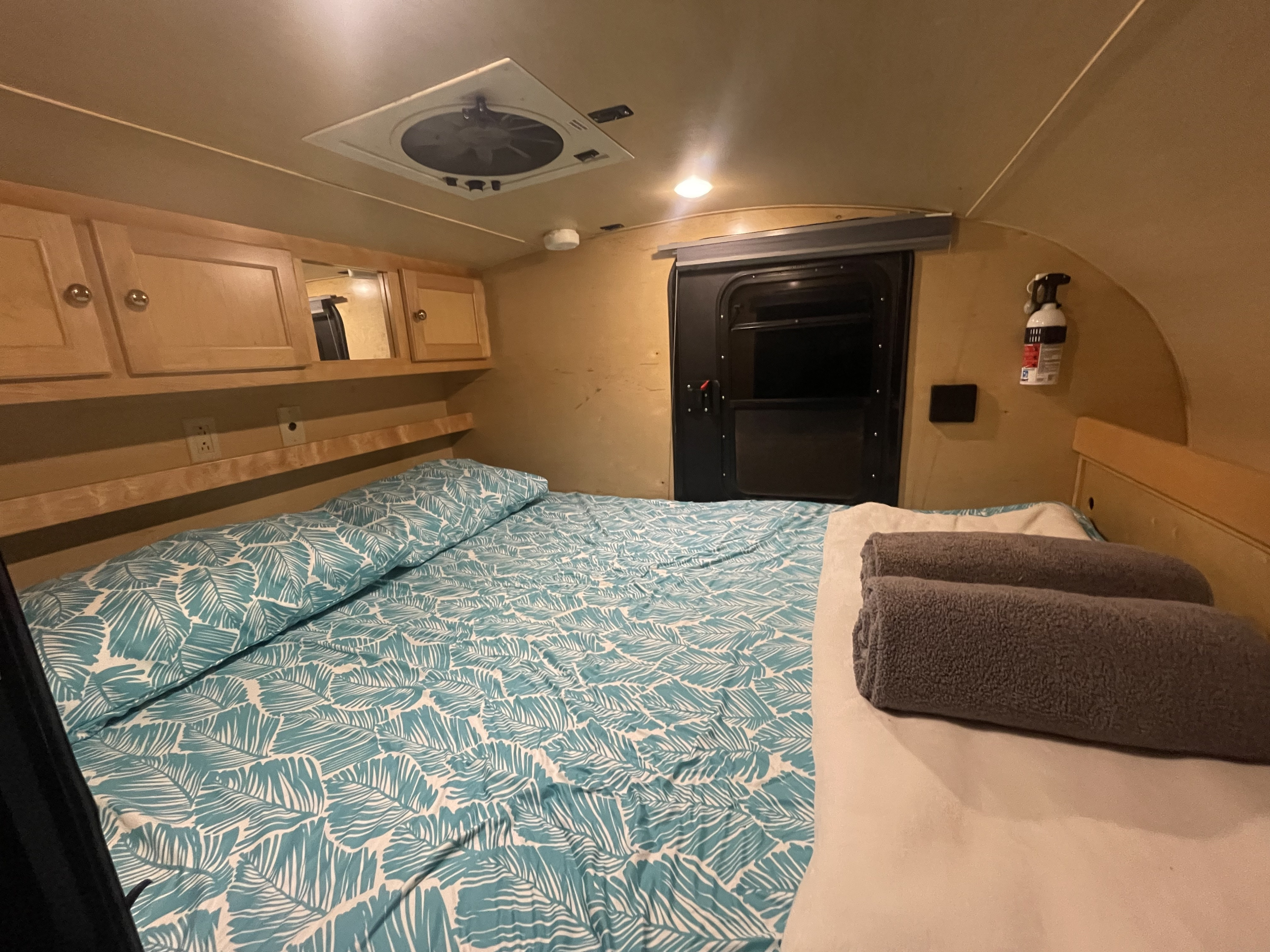 This RV rental features a comfortable bed with leaf-patterned sheets, wooden cabinets, a ceiling fan, and safety equipment.. Little Guy Silver Shadow 2015