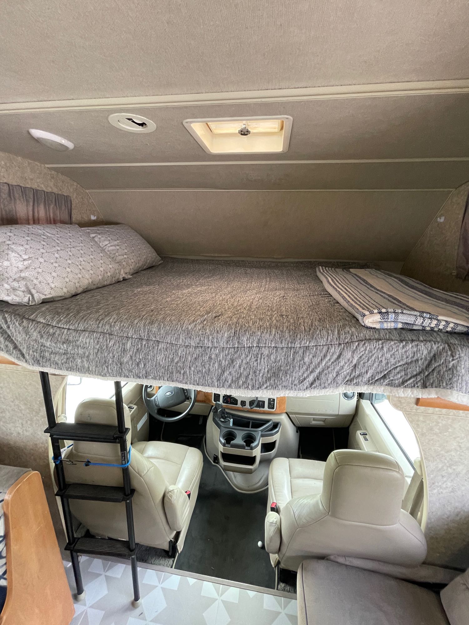 Cozy cab-over bed in an RV rental, showing the ladder access and driver's area.. Winnebago Access 2010