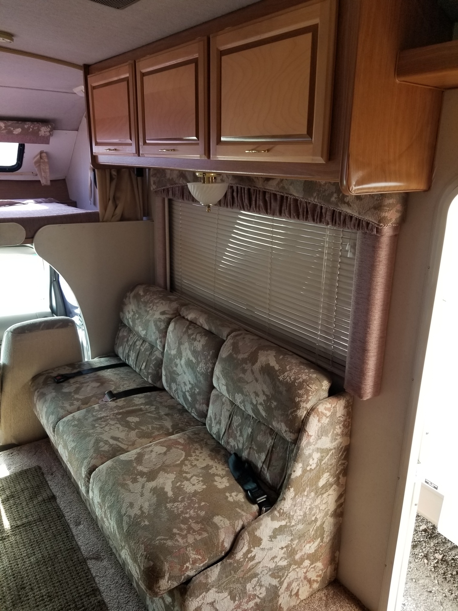 Interior of an RV rental: a floral patterned sofa, wooden overhead cabinets, and window blinds in natural light.. Ford Tioga 1998