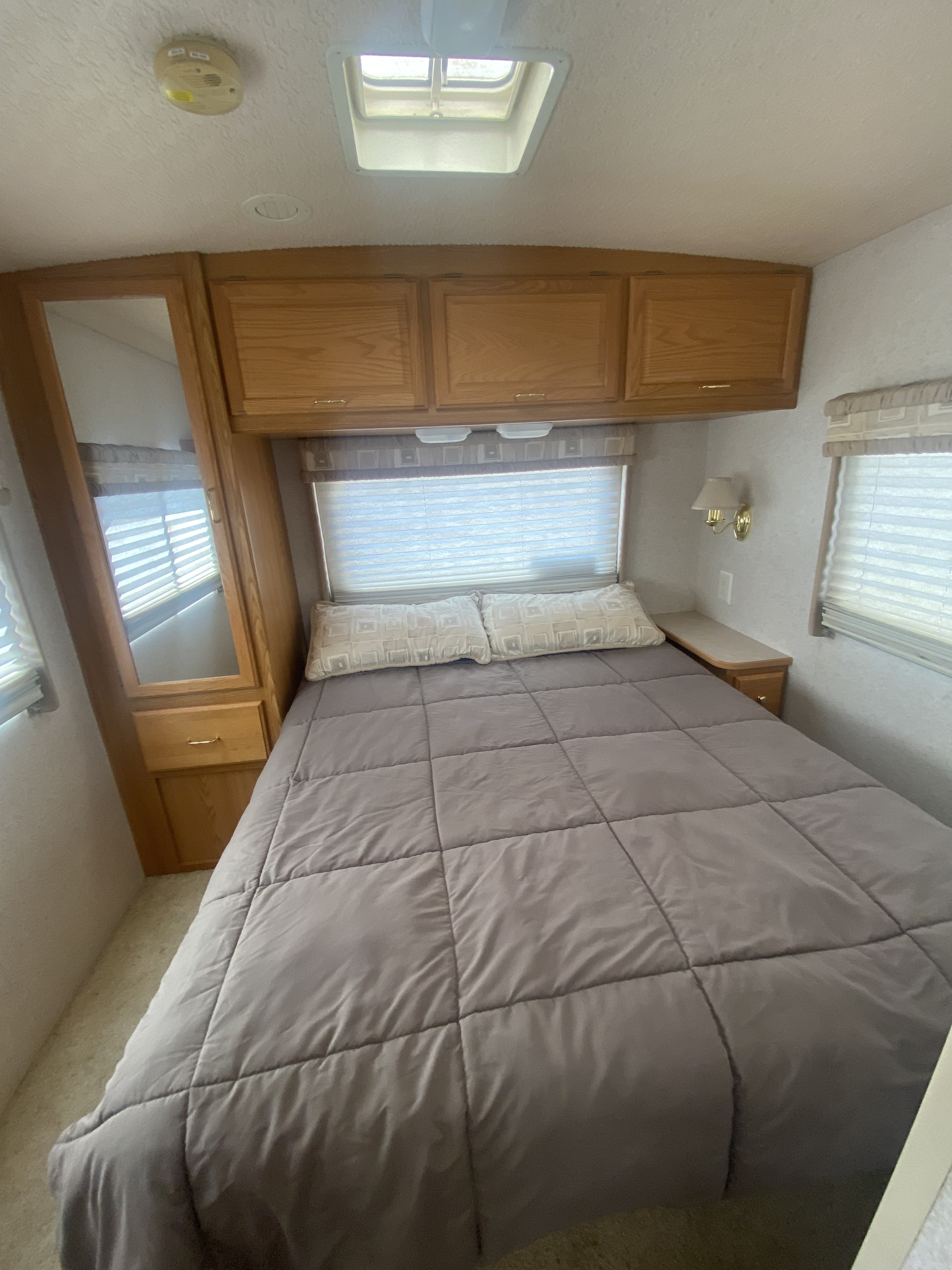 RV rental bedroom with a large, comfy bed, overhead wooden cabinets, bright windows, and a ceiling skylight.. Winnebago Minnie 2004