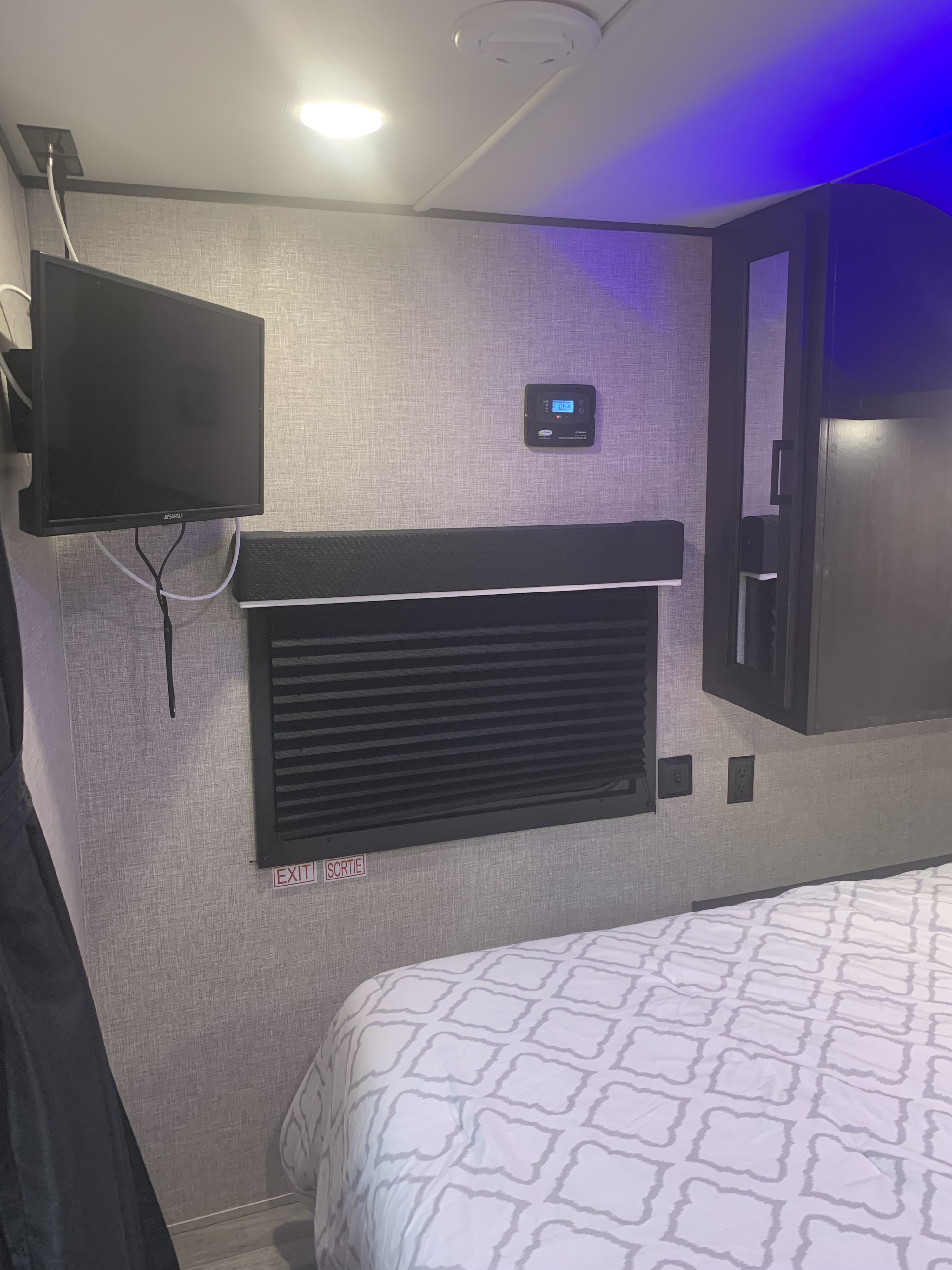 Inside an RV rental: a compact bedroom with mounted TV, solar charge controller, and patterned bed.. Jayco Jay Flight 2022