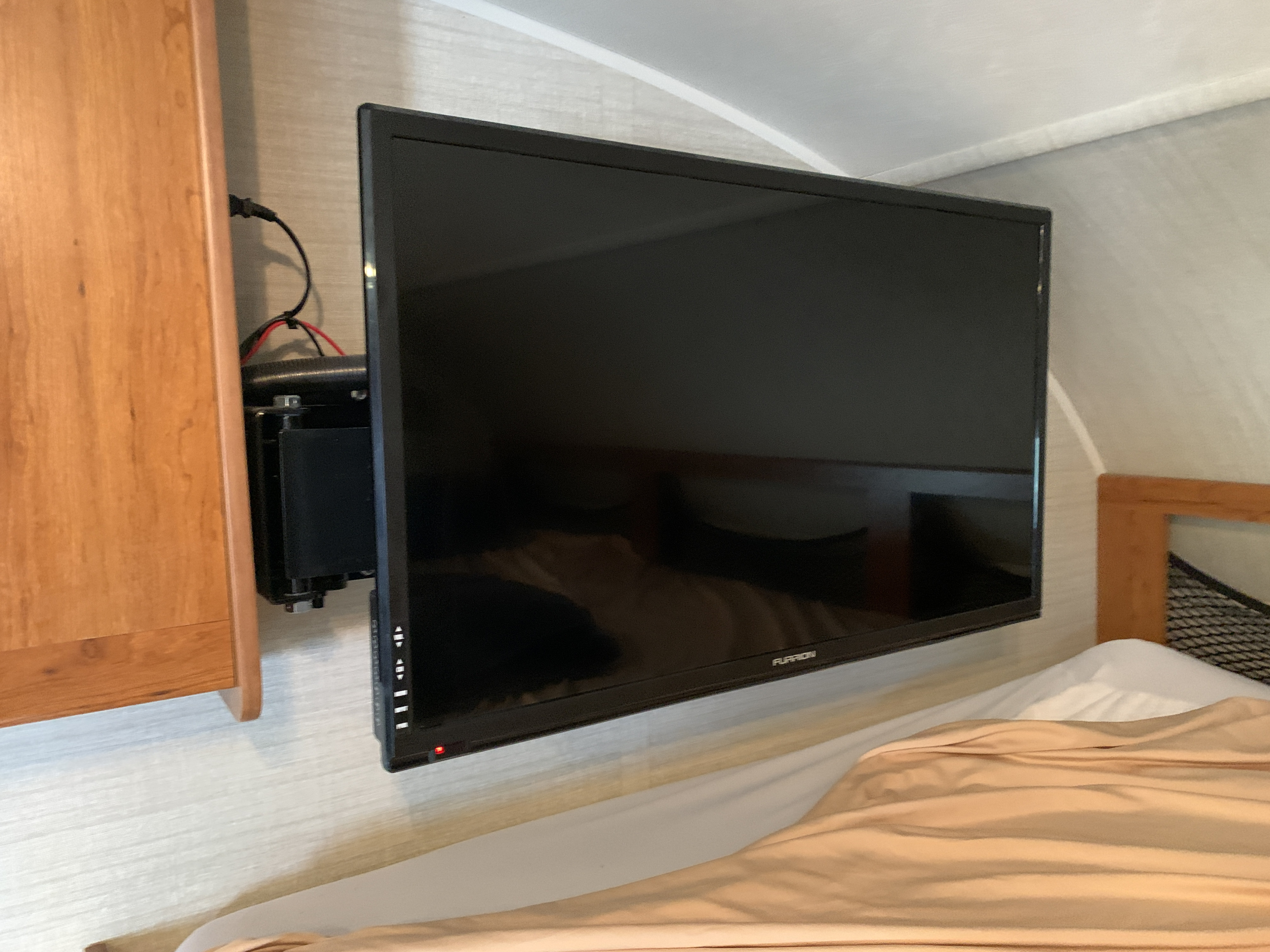 A black Furrion TV mounted on the wall in an RV rental interior, with visible cables and a red power light.. Jayco Redhawk 2017