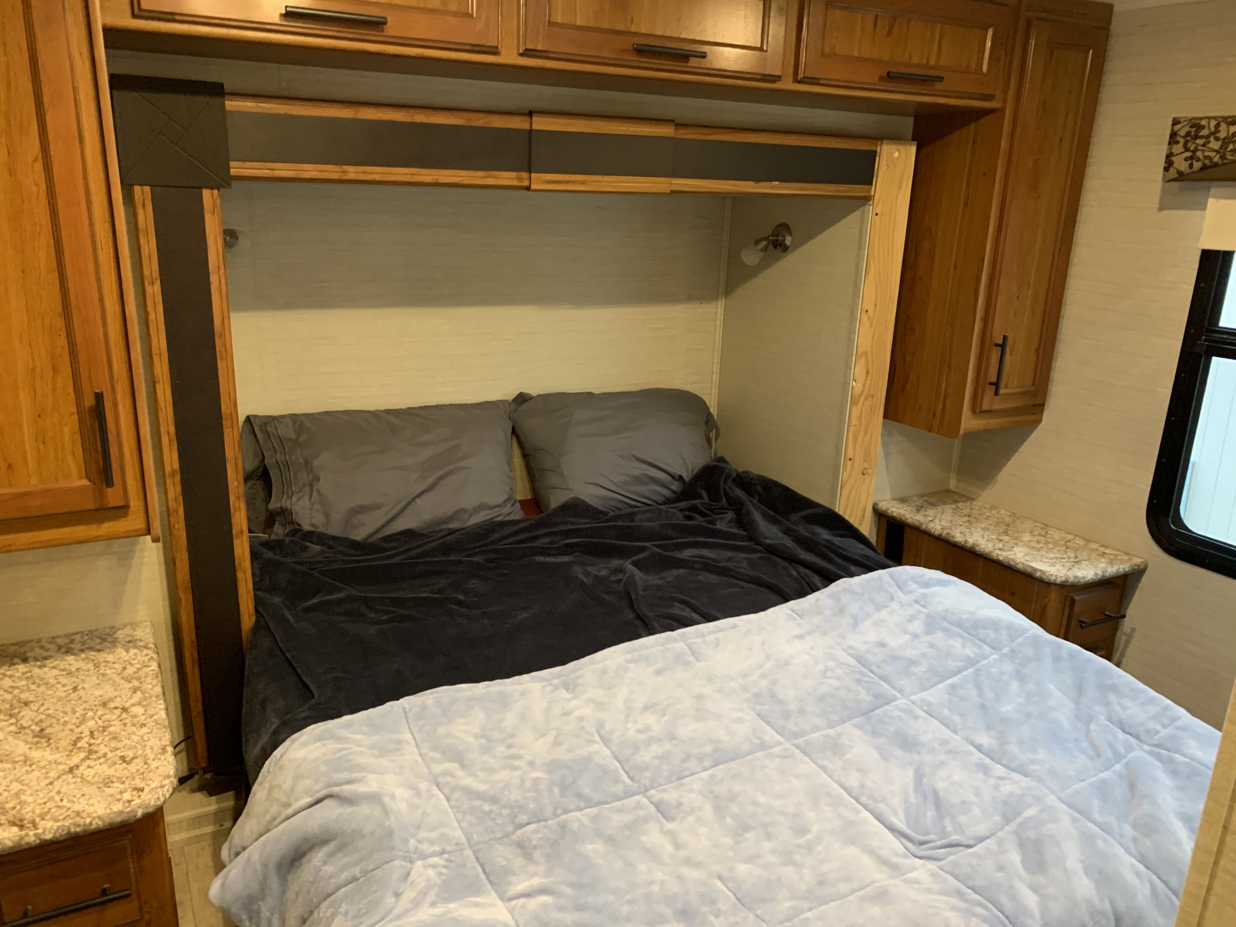 An RV rental bedroom featuring a comfortable bed with light blue and dark grey bedding, grey pillows, and wood cabinetry.. Jayco Redhawk 2017