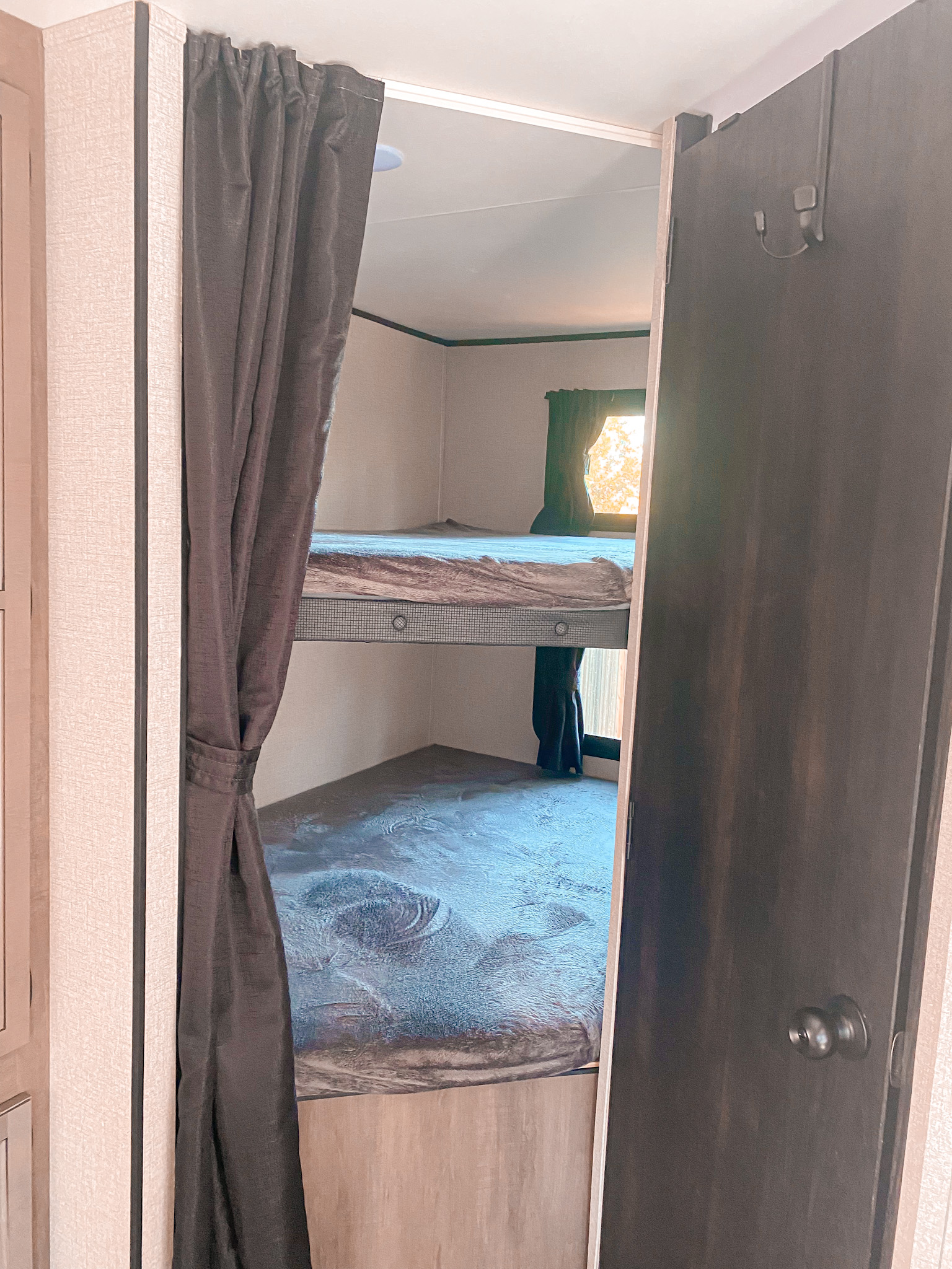 View inside an RV rental showing stacked bunk beds, with a dark curtain on the left and a partially open dark door on the right.. Starcraft Travel Trailer 2022