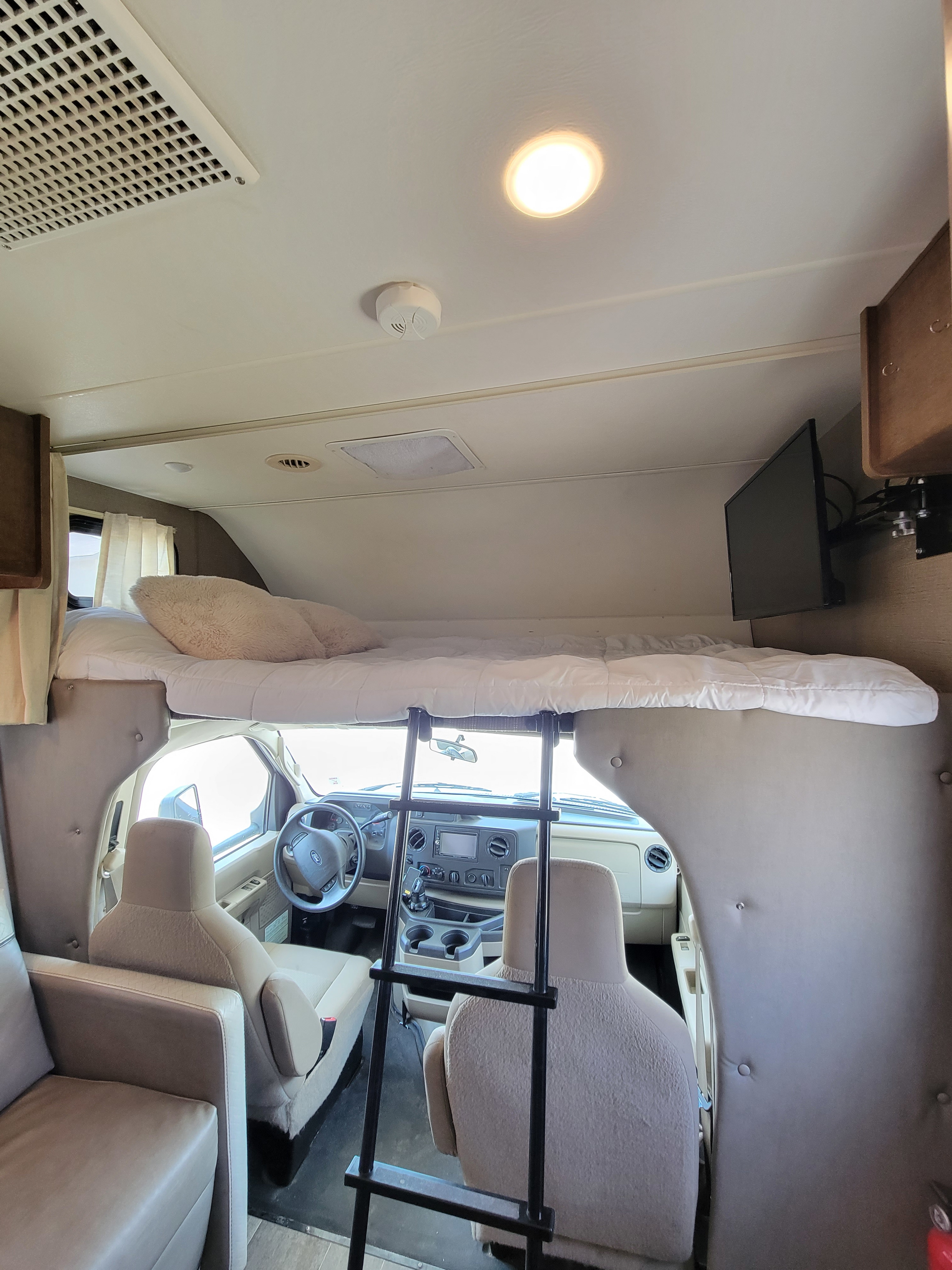 RV rental motorhome interior: driver's cab with ladder to an overhead bed, TV, AC, and comfy seating.. Winnebago Outlook 2019