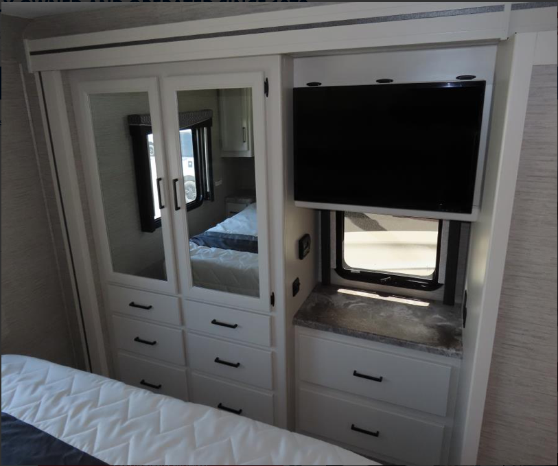 Comfortable RV rental bedroom featuring a white mirrored closet, TV, window, and built-in storage.. Thor Motor Coach ACE 2022