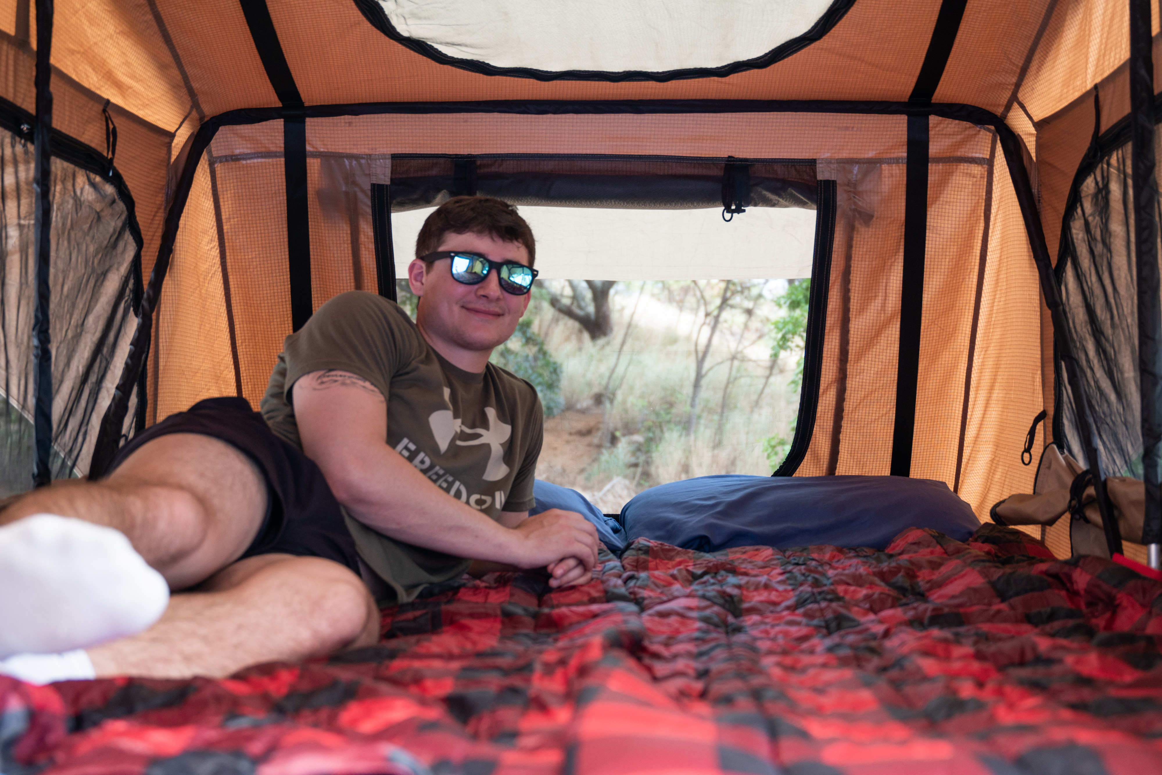 Relaxing inside a spacious **rooftop tent**, part of an **RV rental** adventure. Man smiles, enjoying the **outdoor** comfort.. Toyota Tacoma 2005