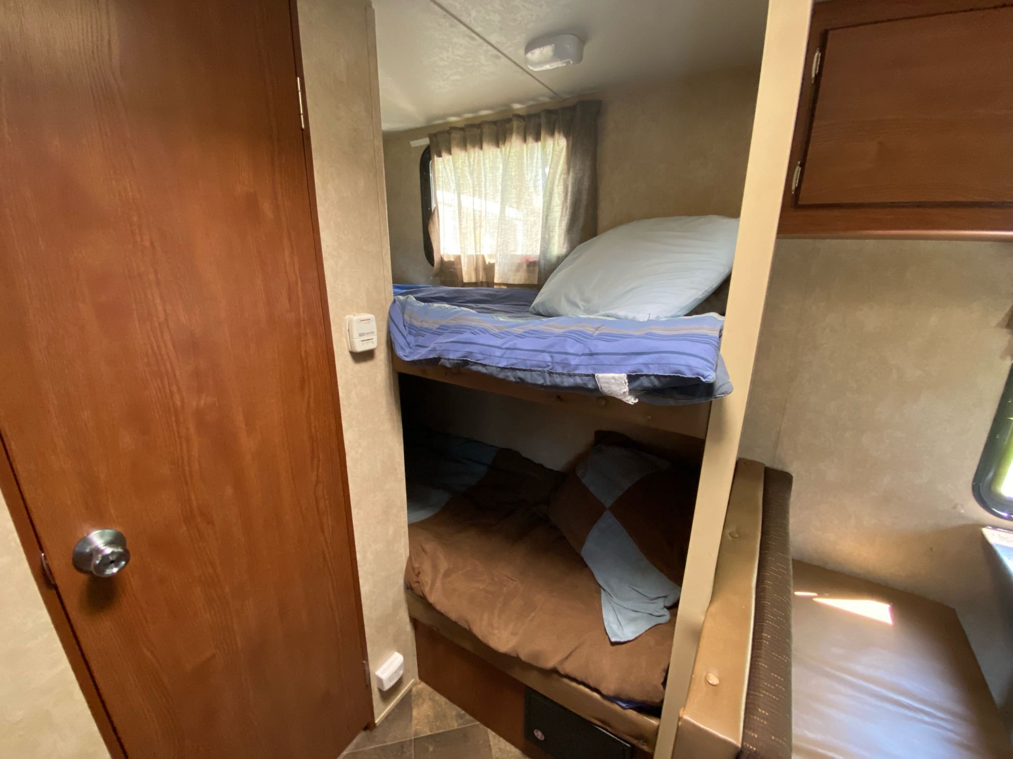 Inside an RV rental: two comfy bunk beds with blue and brown bedding, a door, and window.. Forest River Salem Cruise Lite 2015