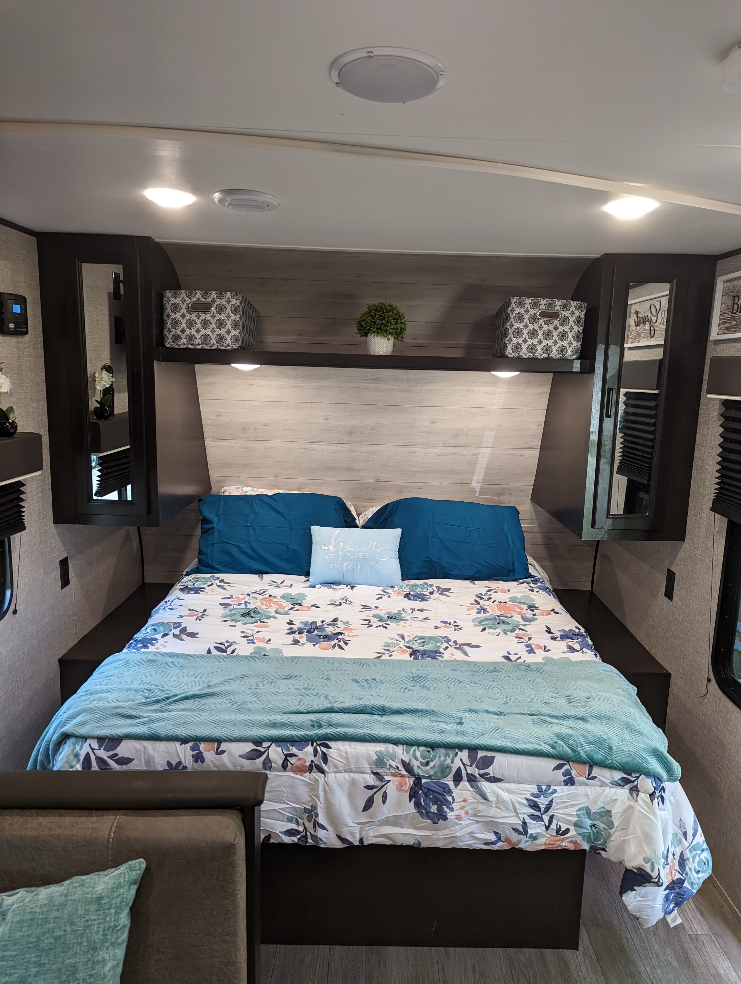 Cozy RV rental bedroom with floral and teal bedding, featuring overhead storage, built-in lighting, and dark wood accents.. Jayco 224BHW 2022