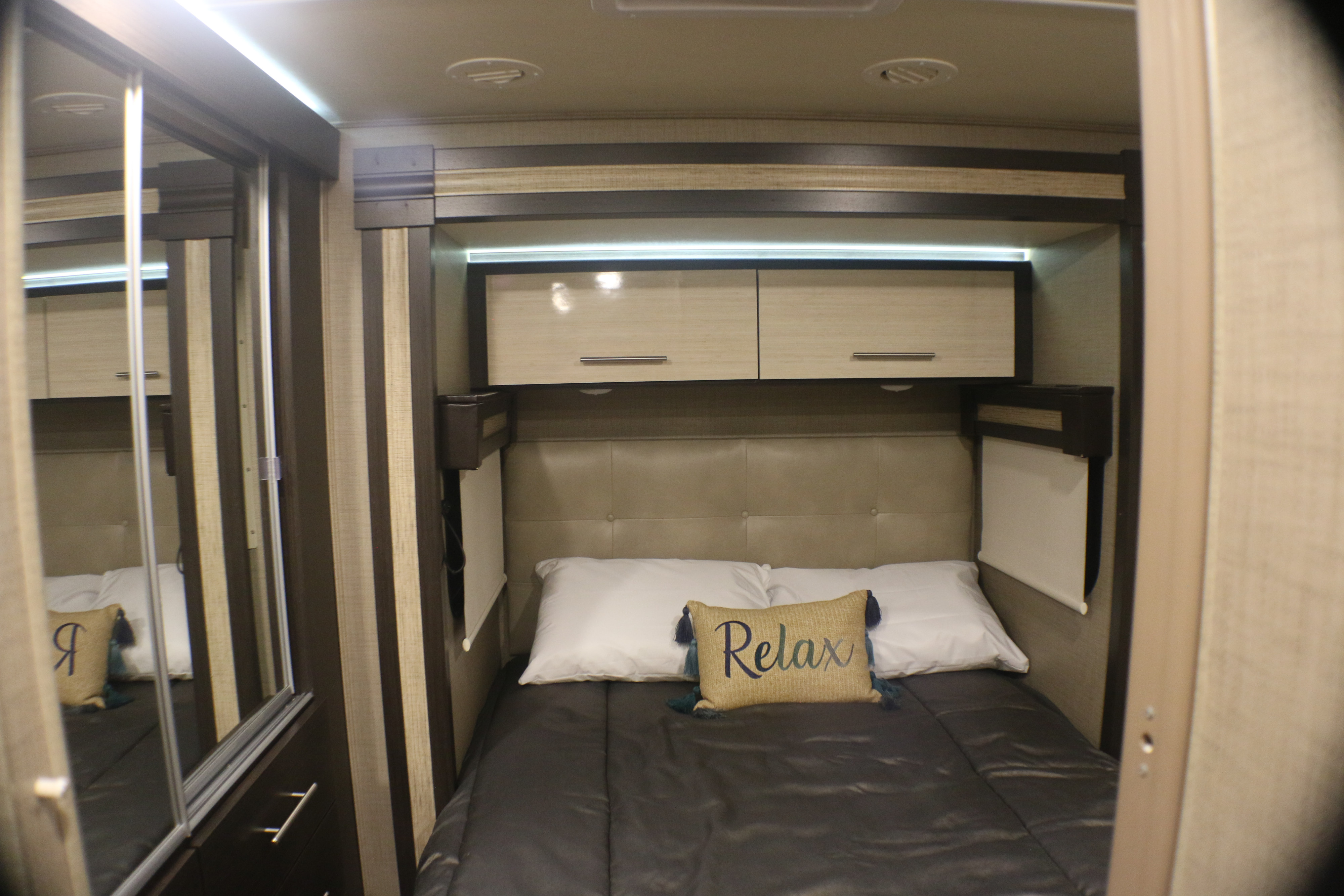 Comfortable RV rental bedroom with a "Relax" pillow, overhead storage, and mirrored closet, offering a cozy space for your journey.. Thor Gemini 2020