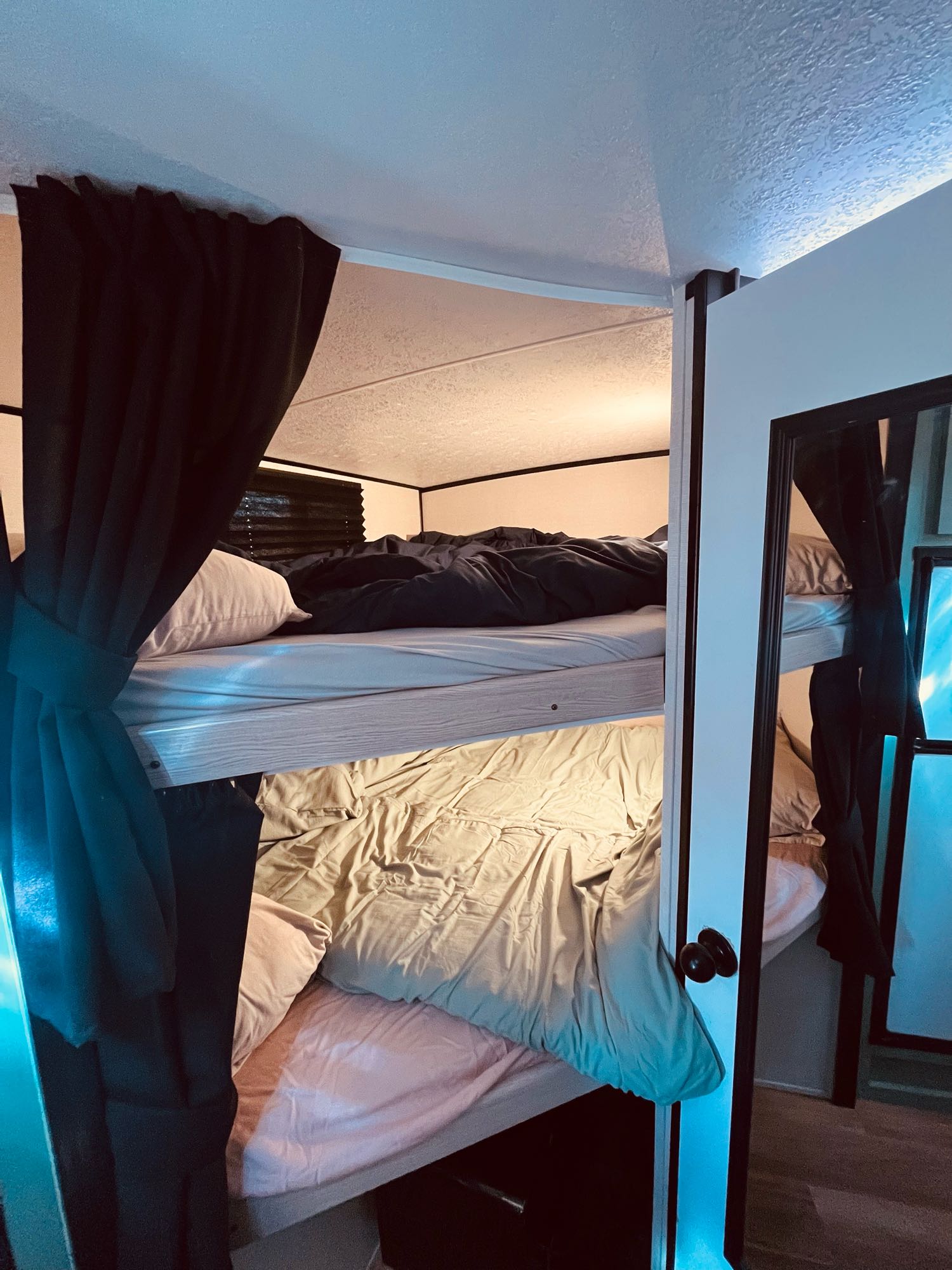Inside an RV rental: two compact bunk beds with bedding. Curtains and a mirror enhance the cozy sleeping area.. Forest River Coachmen Apex Nano Off-Grid 2022