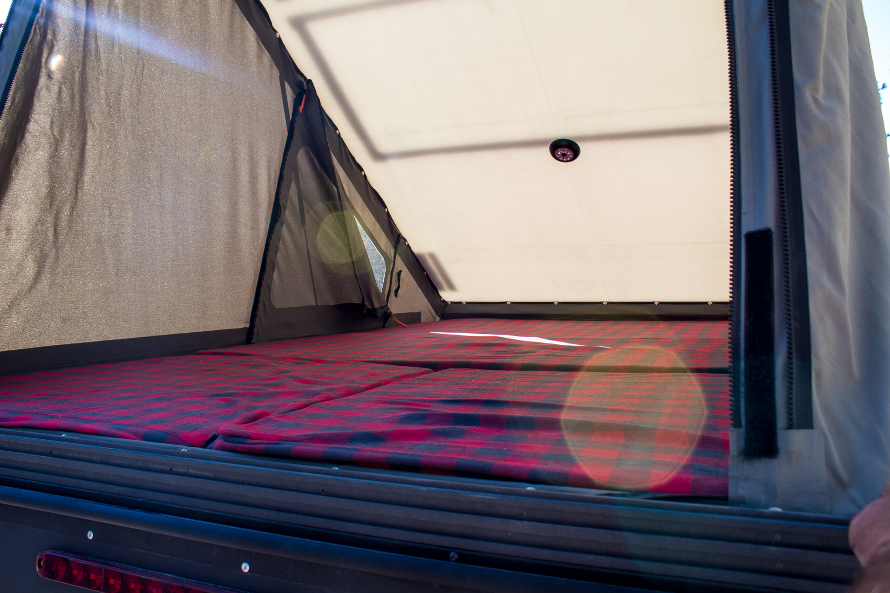 Your RV rental adventure awaits! A cozy, well-lit sleeping area with a red plaid mattress in a pop-up tent.. Ram Power Wagon 2020