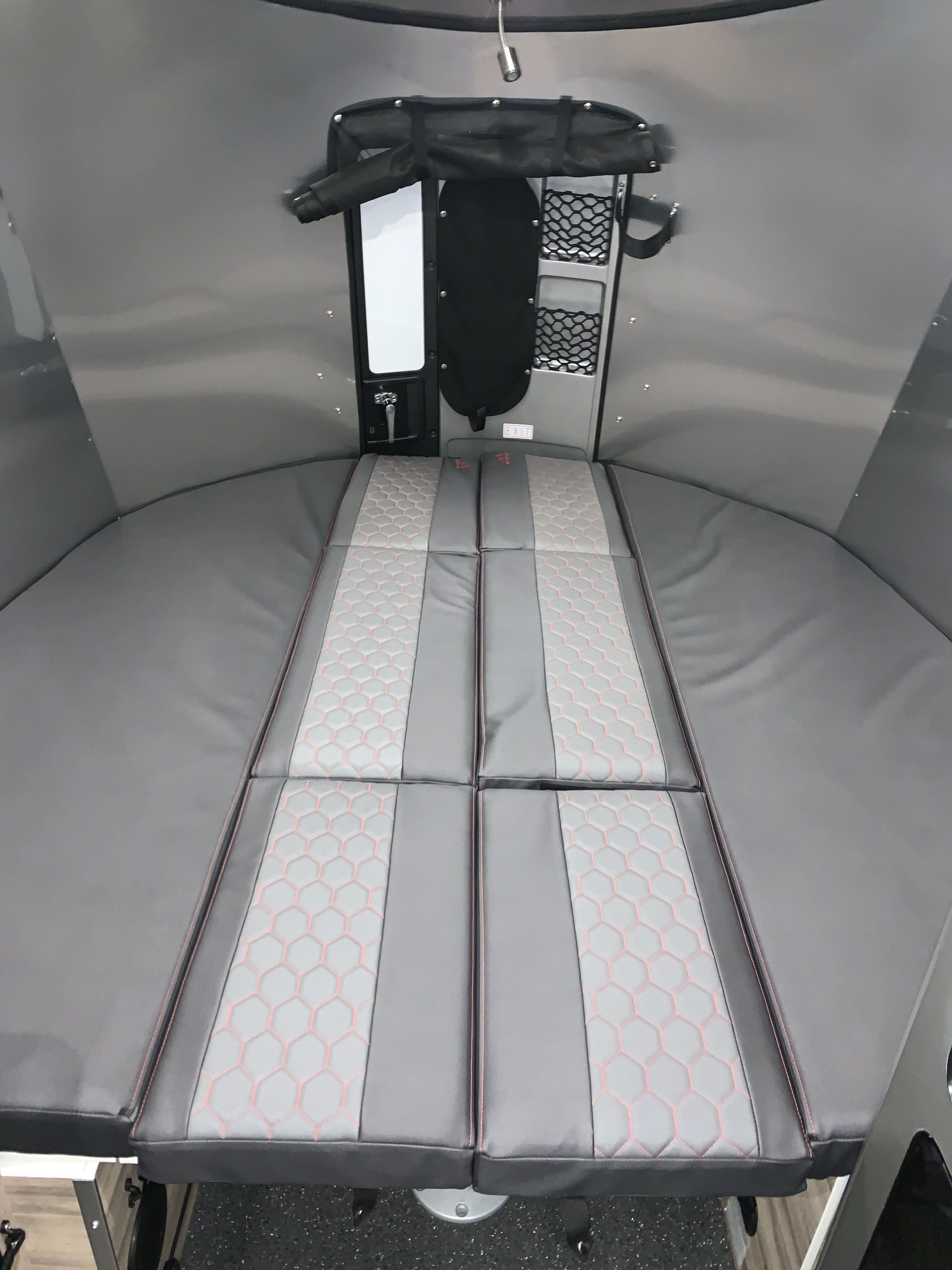 RV rental interior: A cozy gray sleeping area with patterned cushions, overhead storage, and integrated light.. Airstream Basecamp 2021