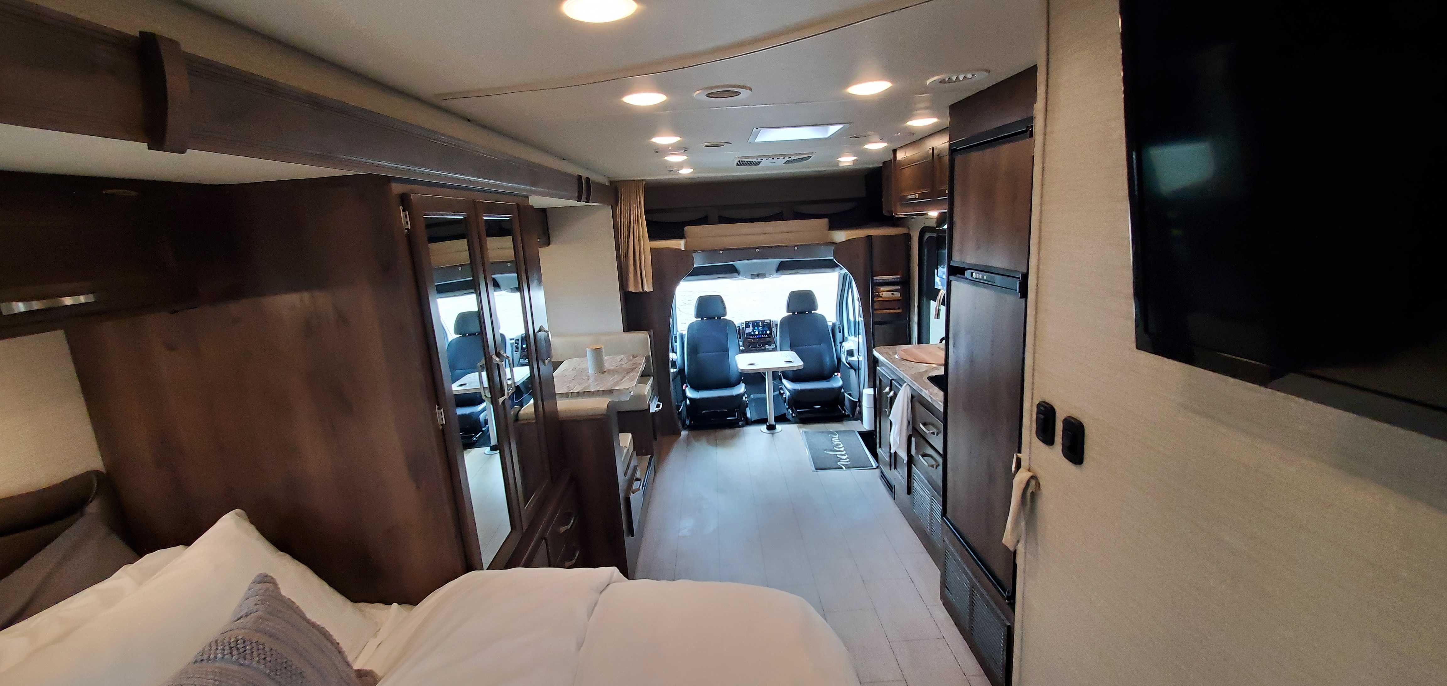Interior of an RV rental: a wide shot showing the bed, a compact kitchen on the right, a dinette on the left, and the front cockpit.. Jayco Melbourne 2019