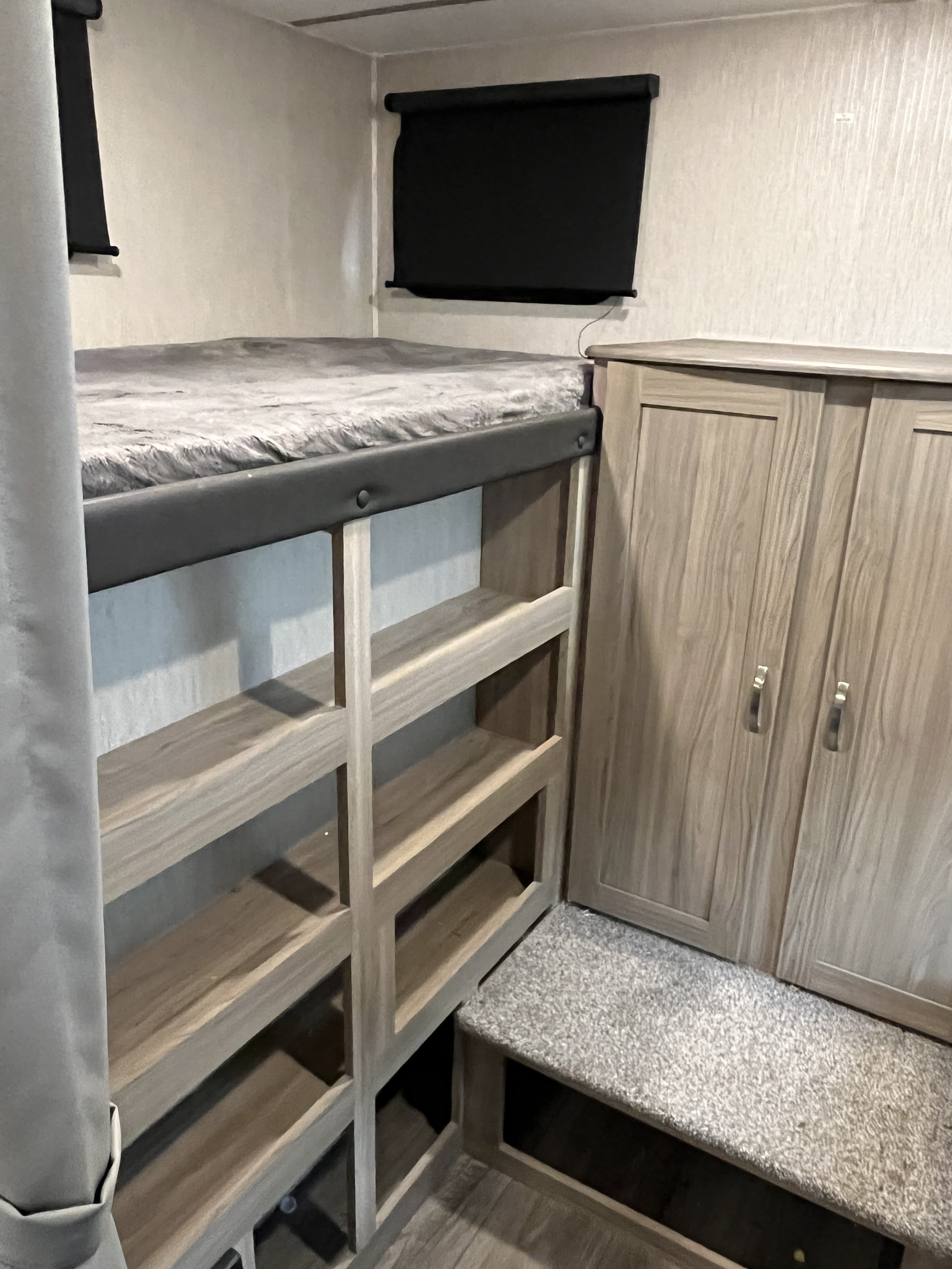 RV rental interior featuring a cozy bunk bed, built-in storage shelves, and a wooden wardrobe cabinet.. Coachmen Freedom 2021