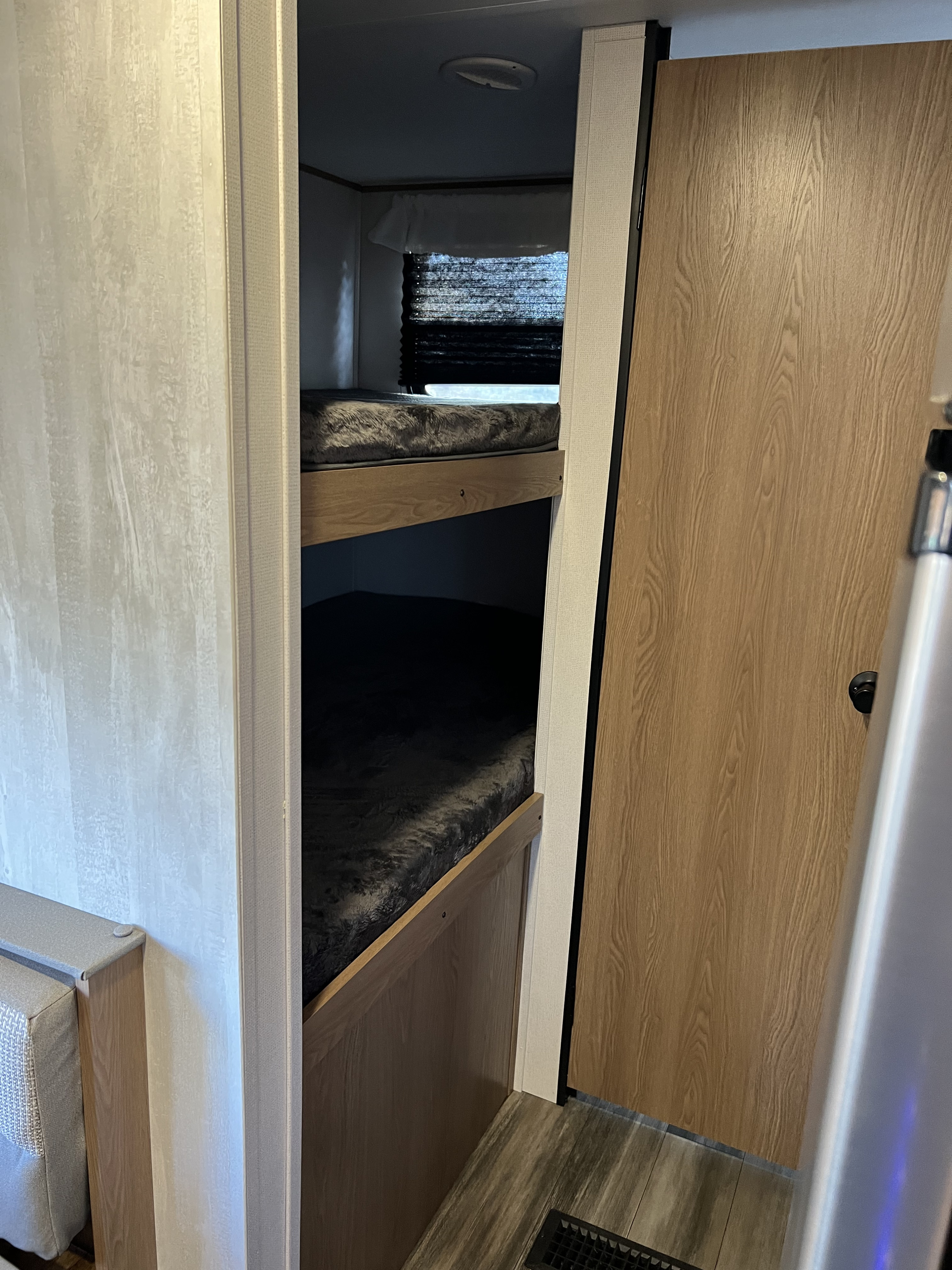 Interior of an RV rental featuring cozy bunk beds with dark blankets and wood trim, ideal for family trips.. Avenger other 2022