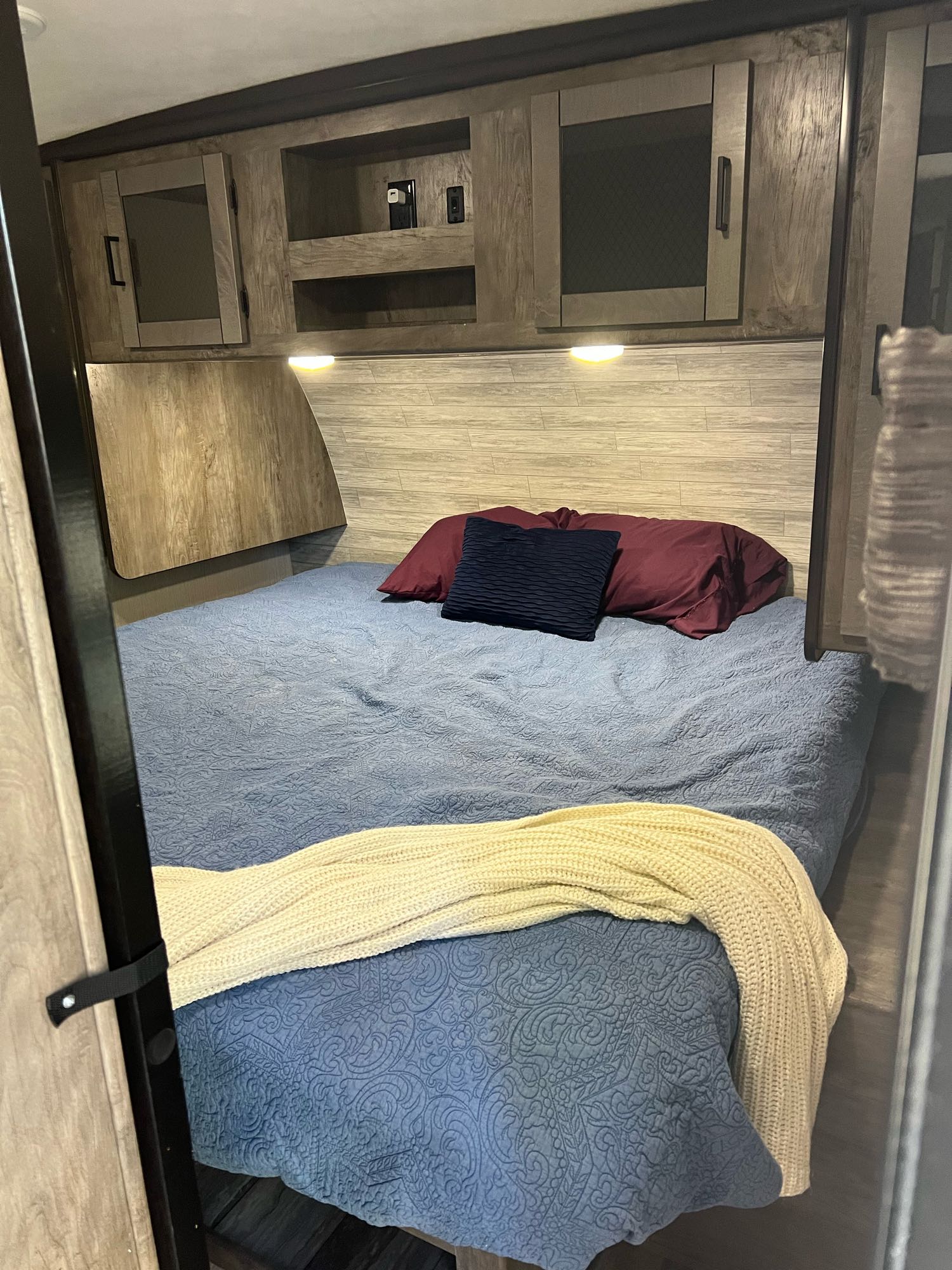 Cozy RV rental bedroom with blue quilted bed, pillows, overhead storage, and reading lights for comfortable travel.. Heartland North Trail 2020
