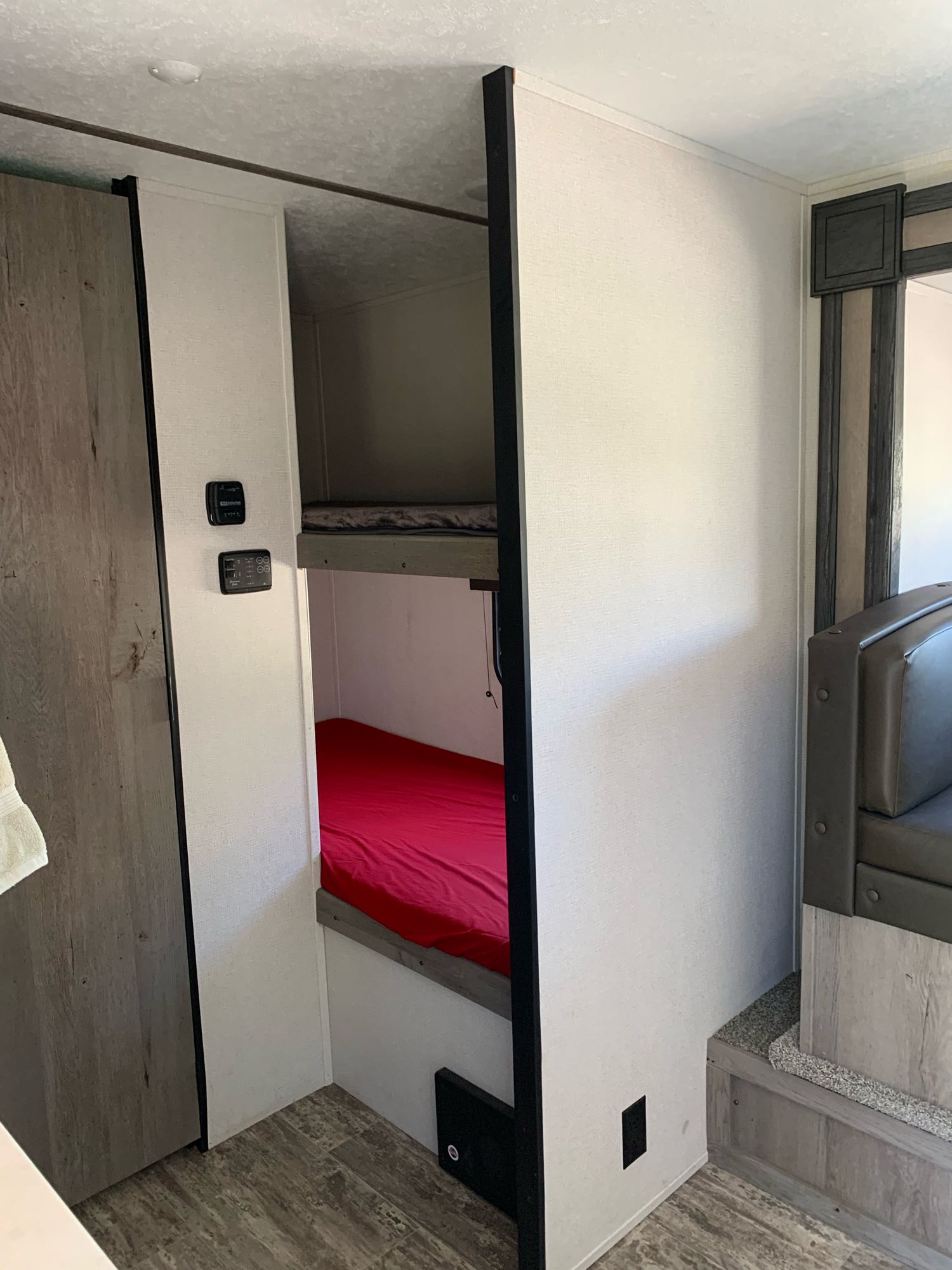 This RV rental interior features stacked bunk beds, one with a red bedspread, next to a wood-look doorway and a diner-style booth.. Springdale Bunkhouse 2021