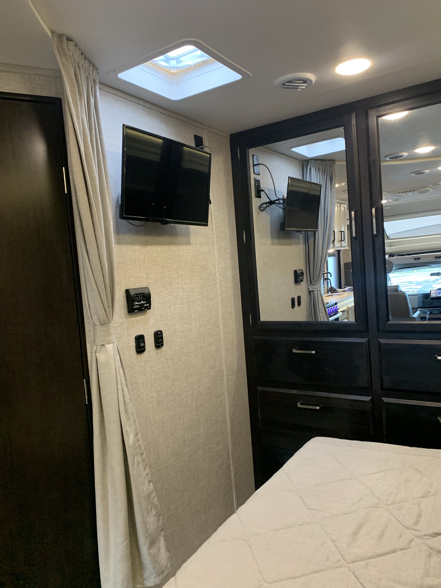 Inside an RV rental: a compact bedroom area with a mounted TV, mirrored wardrobe, and overhead skylight.. Entegra Odyssey 2022