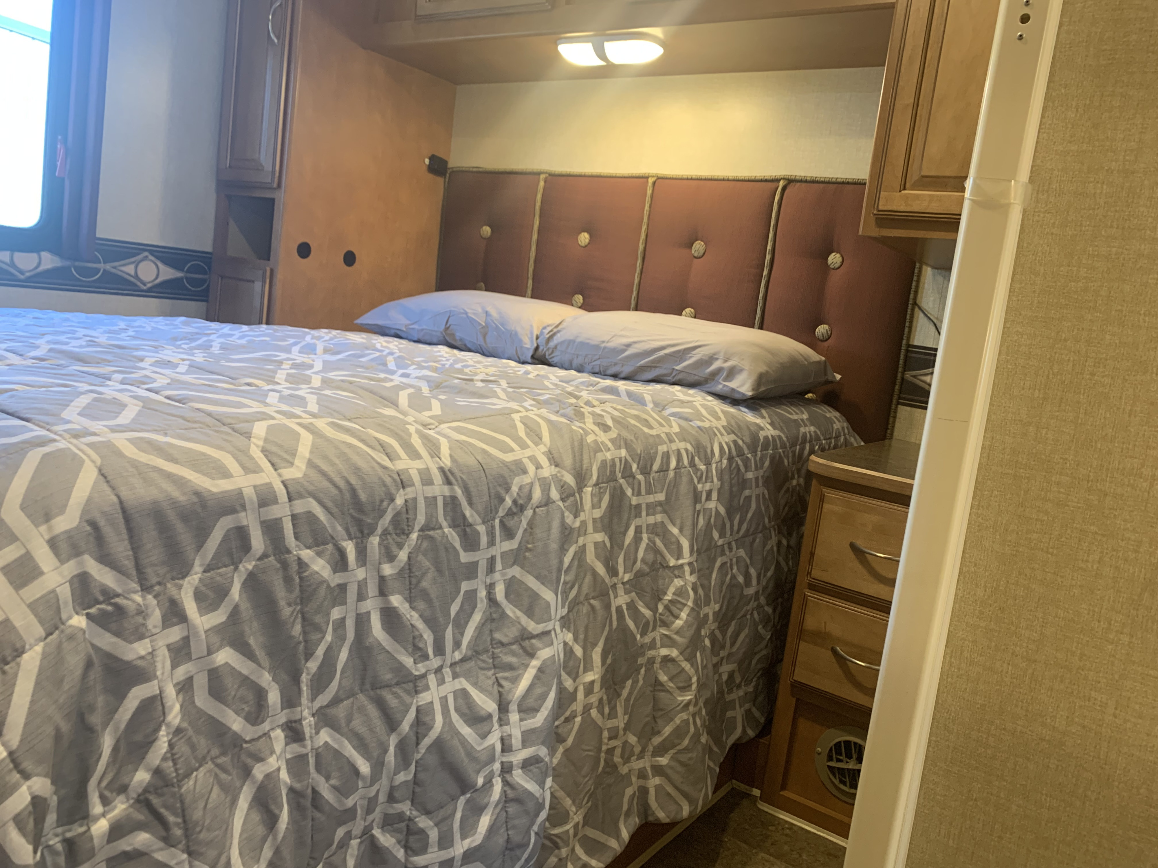 Inviting RV rental bedroom with a bed featuring a geometric comforter, tufted headboard, and built-in wood storage.. Winnebago Minnie Winnie 2016