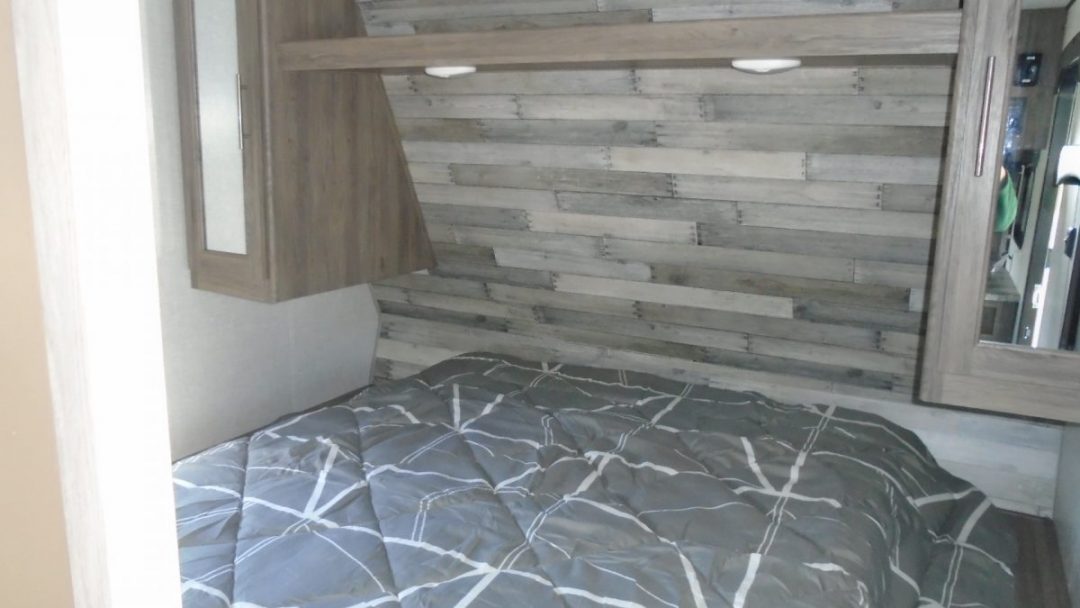 RV rental: Cozy bedroom with a gray patterned bed, rustic wood-paneled wall, and convenient overhead storage.. Crossroads RV Zinger 2022