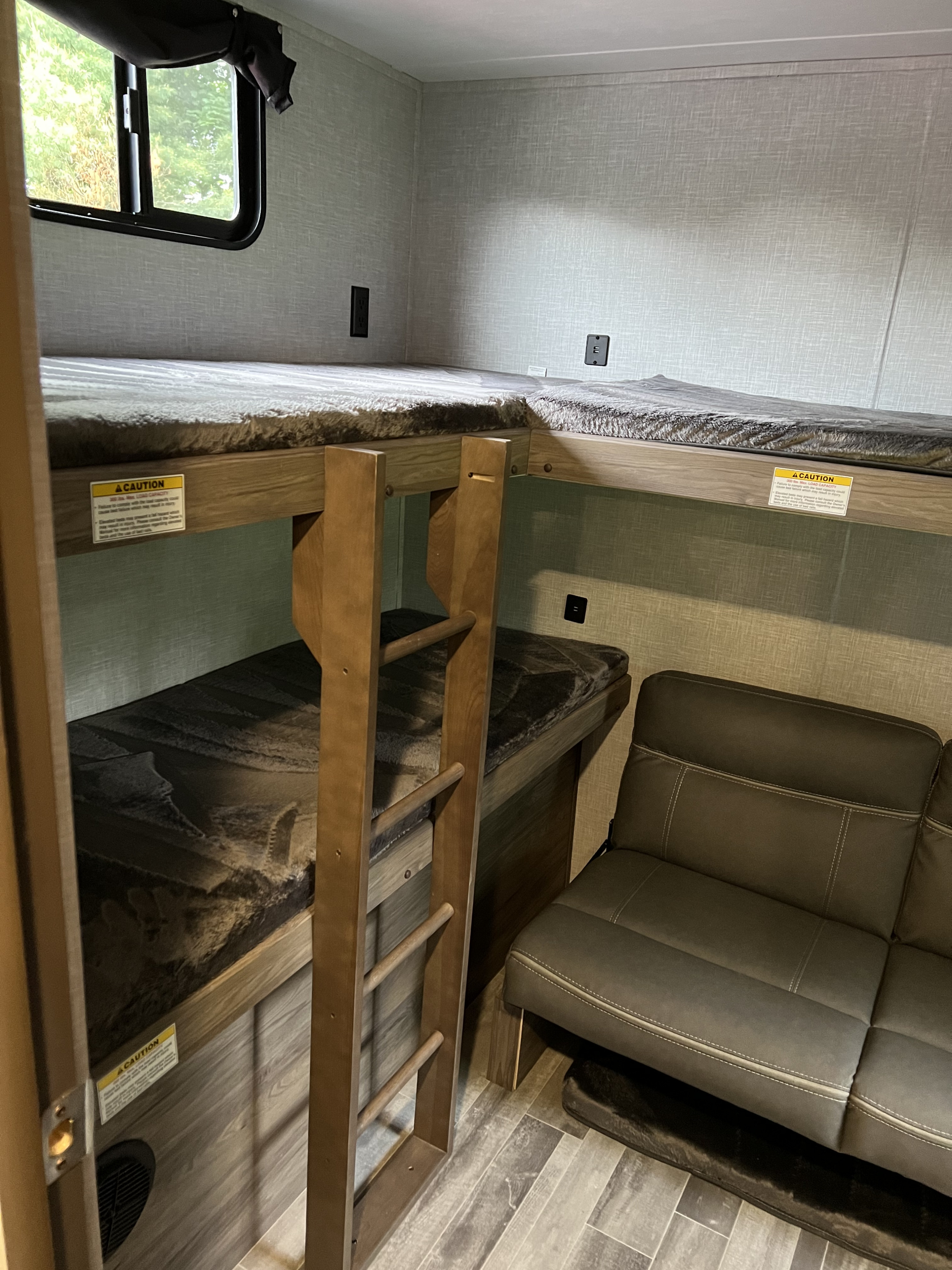 RV rental interior with stacked wooden bunk beds, a ladder, and a brown sofa for extra sleeping and seating.. Crossroads RV Zinger 2022