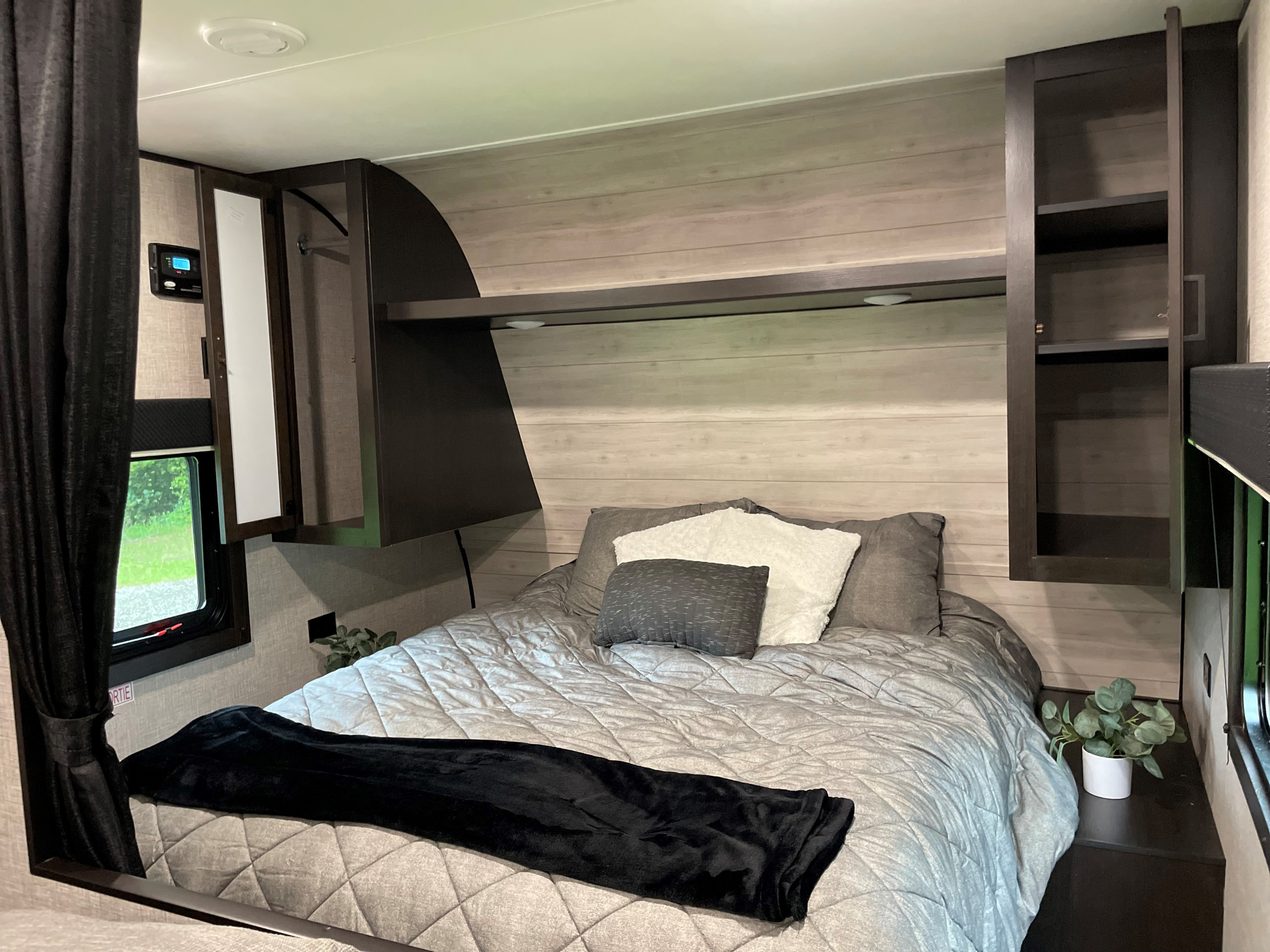 A well-appointed RV rental bedroom, featuring a comfortable bed, overhead storage, and light wood-look wall panels.. Jayco Jay Flight 2022