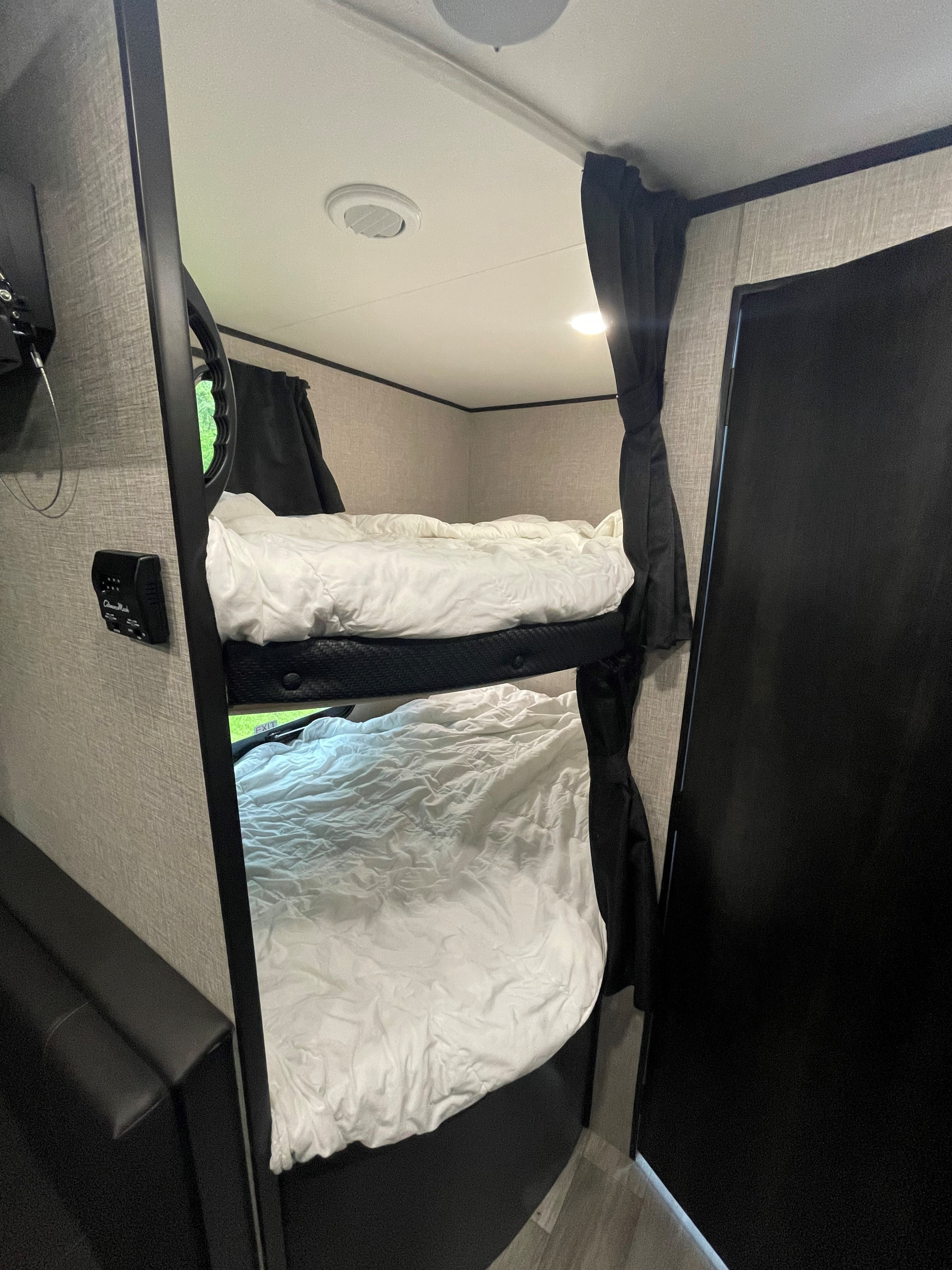 Inside an RV rental: two made-up bunk beds with white bedding, a wall-mounted TV, and an AC control panel.. Jayco Jay Flight 2022