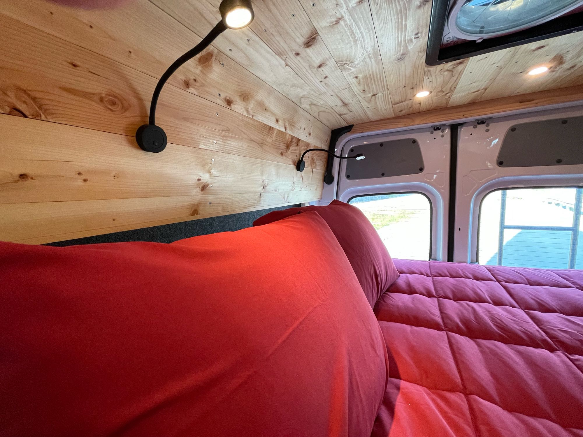 Cozy RV rental interior featuring a comfy red bed, natural wood paneling, and adjustable reading lights.. Mercedes Freightliner Sprinter 2021