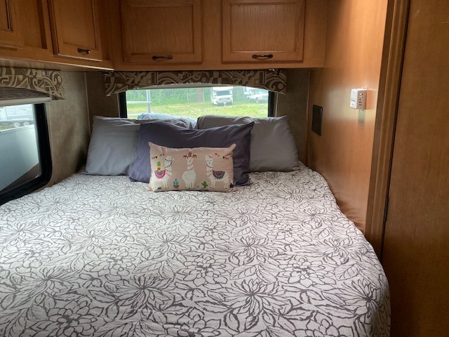 An inviting RV rental bedroom with a bed, patterned comforter, soft pillows, and wooden cabinets, offering cozy travel accommodation.. Coachman Freelander 2013
