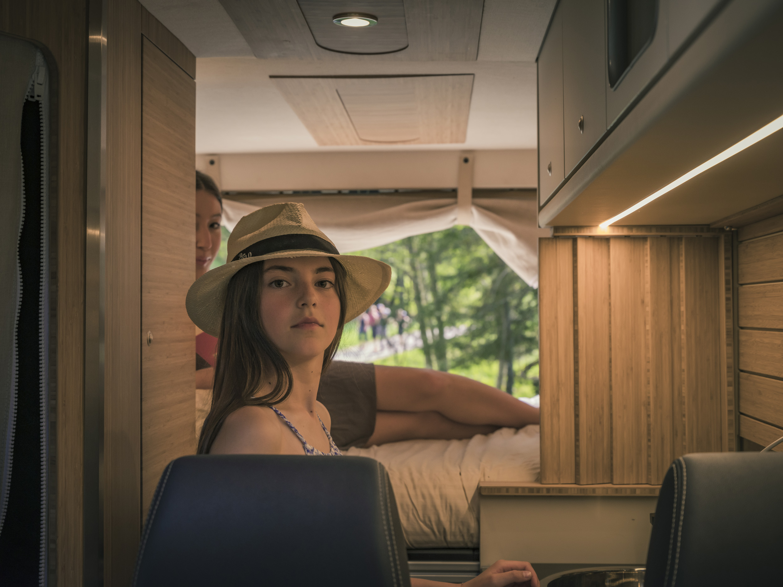 Young girl wearing a hat inside an RV rental, looking towards the viewer. Features a modern, wood-paneled camper interior.. Fiat Ducato MH2 2020