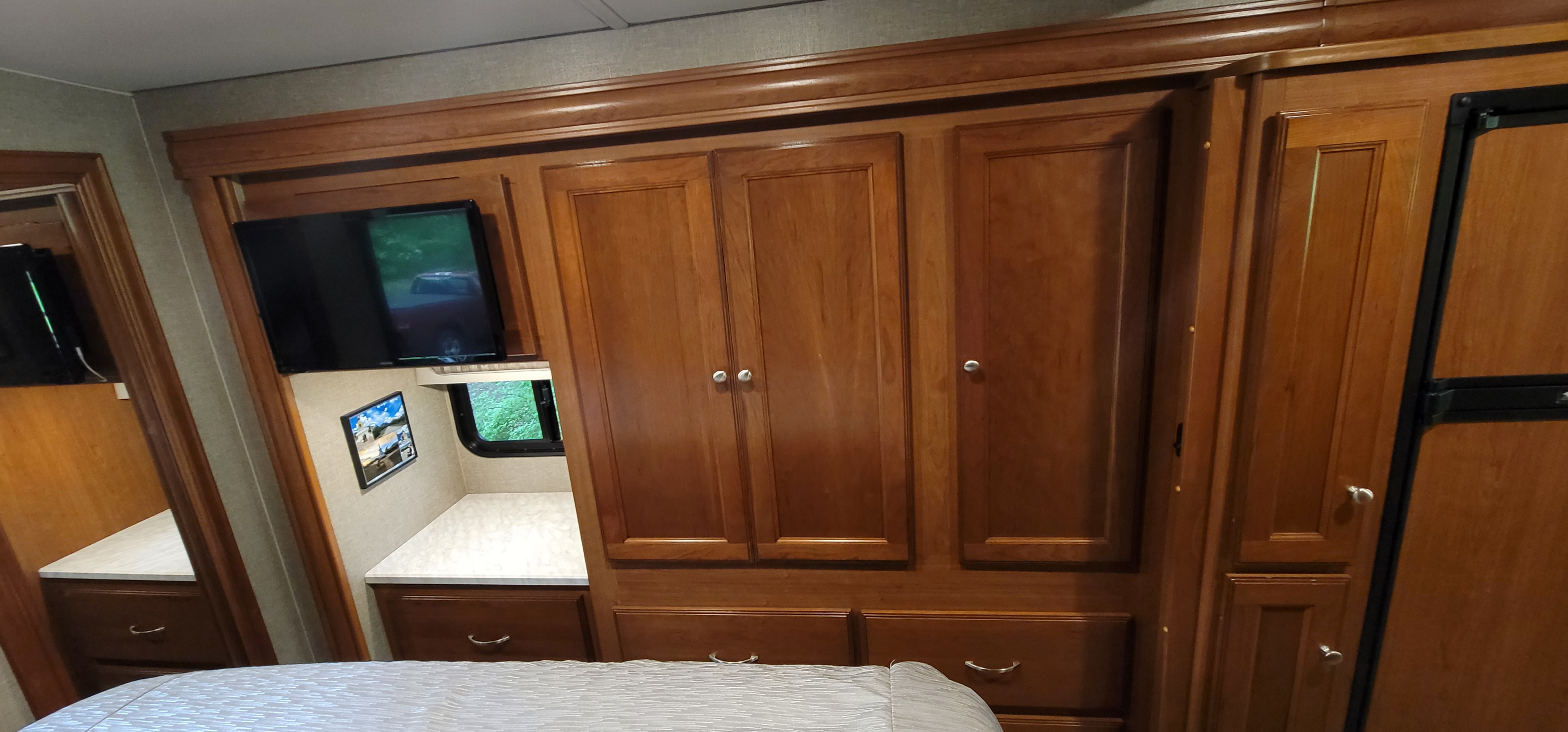 RV rental bedroom featuring warm wood cabinetry, TV, window, and a built-in fridge.. Winnebago Vista 2019