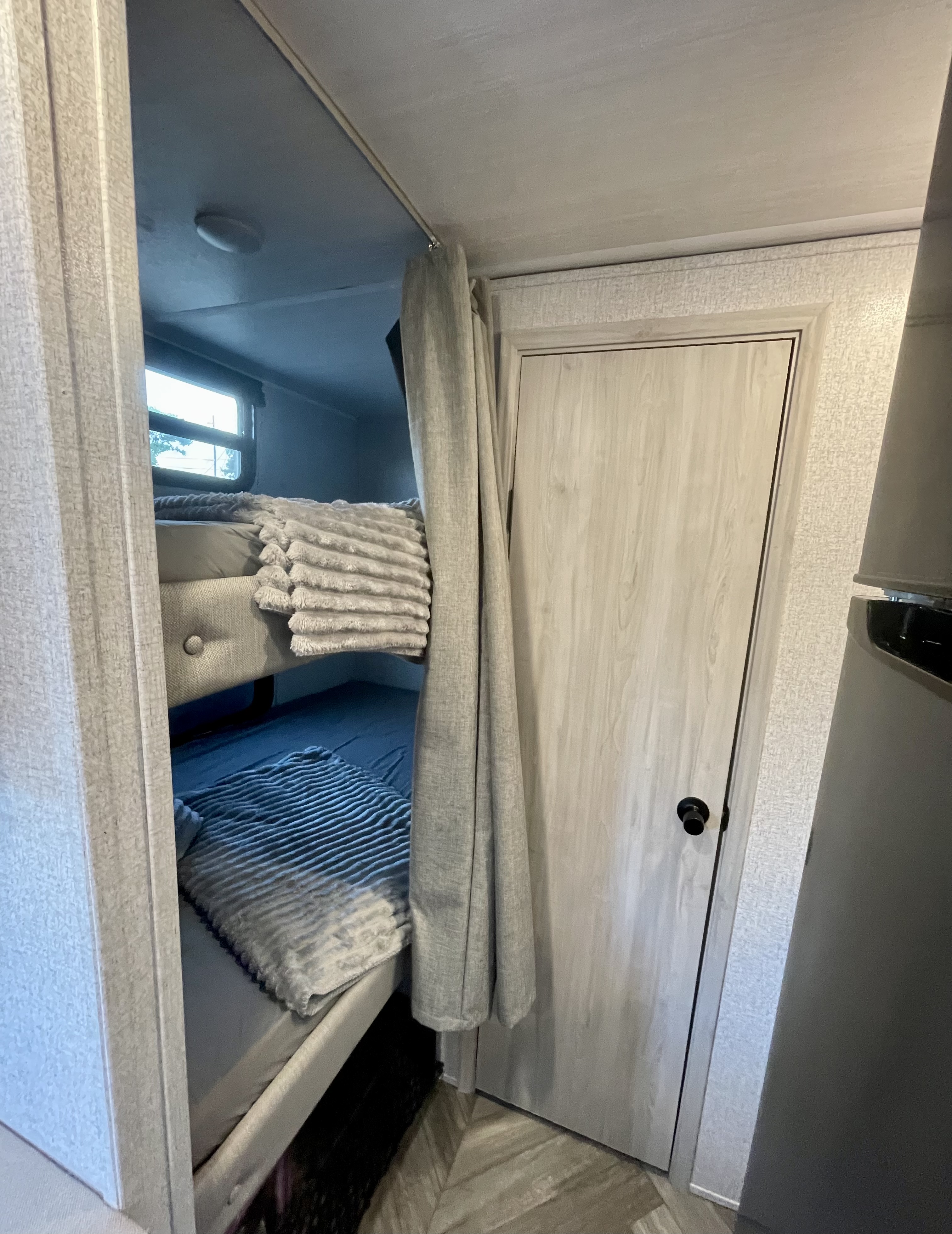 Cozy RV rental bunk beds on the left, separated by a light gray curtain, with a white door on the right.. East to West Della Terra 2022