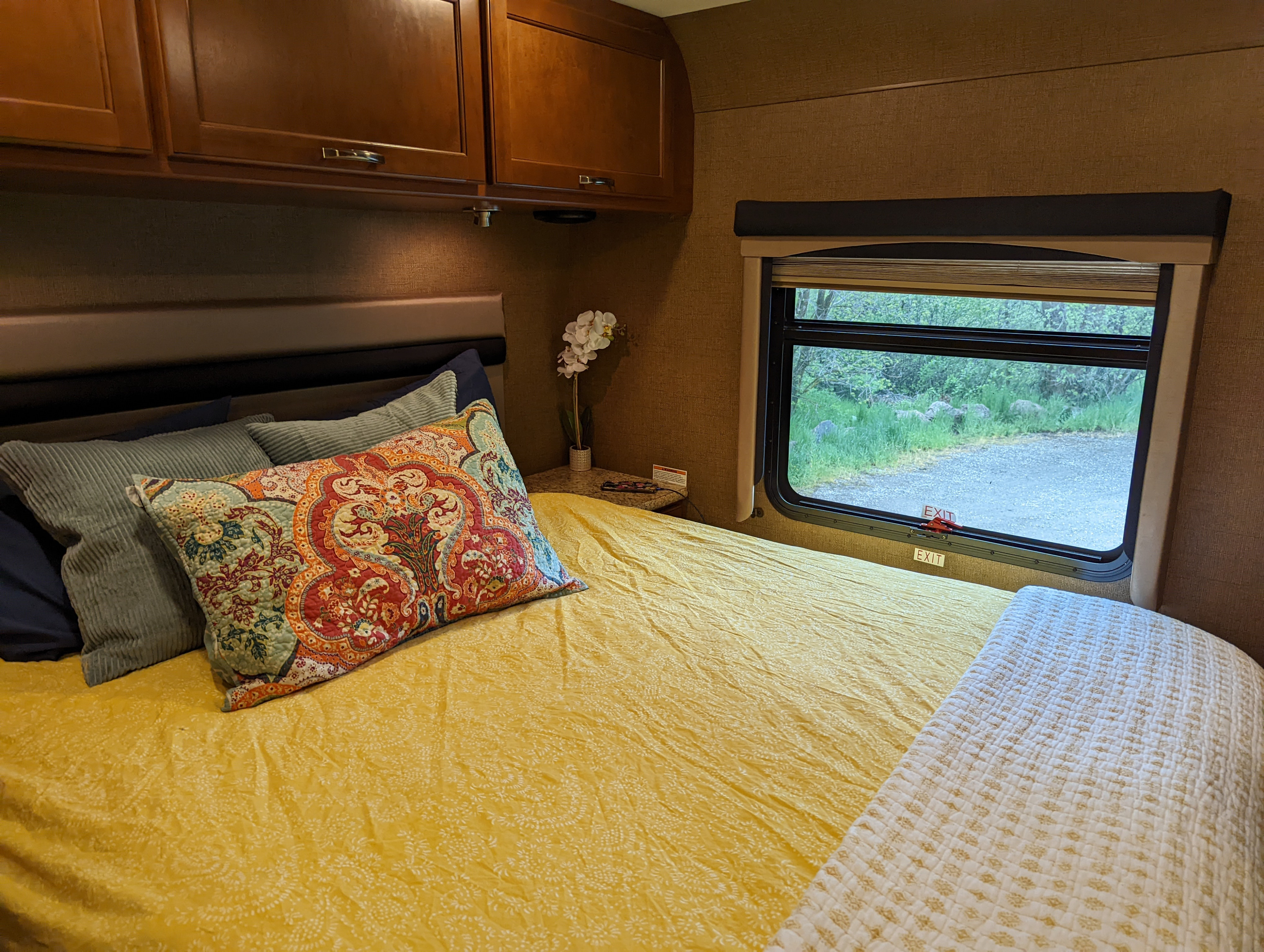 Cozy RV rental bedroom with patterned pillows, overhead cabinets, and a scenic window view.. Thor A.C.E. 2016