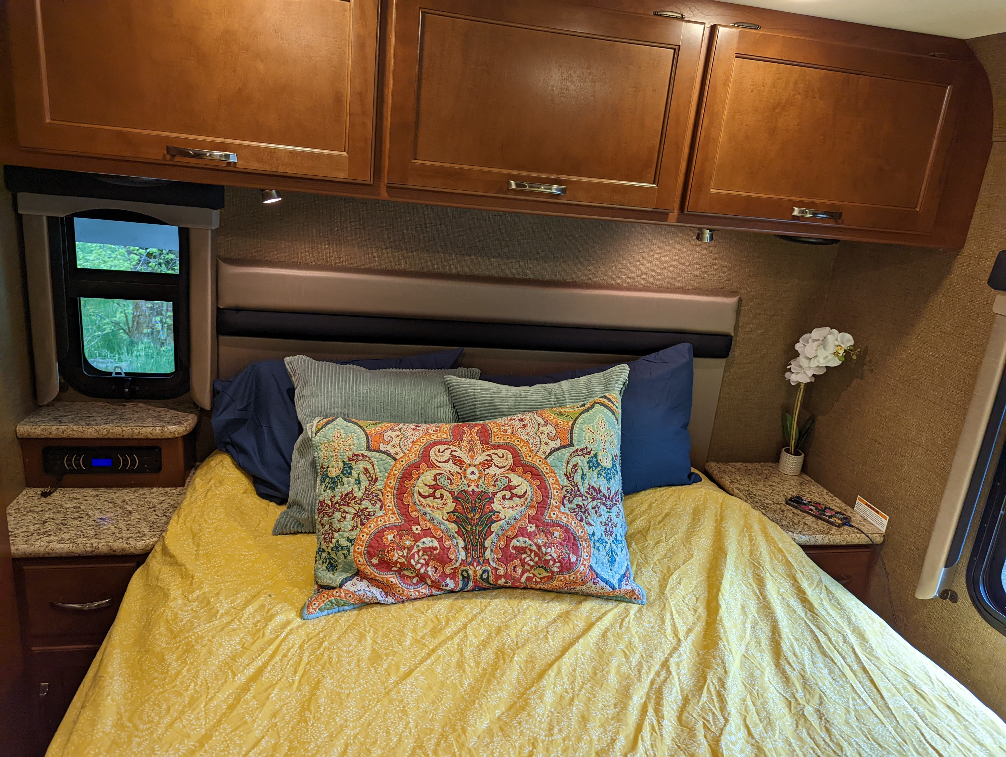 RV rental interior: A cozy bedroom with a vibrant yellow bed, decorative pillows, overhead wooden cabinets, and convenient nightstands.. Thor A.C.E. 2016