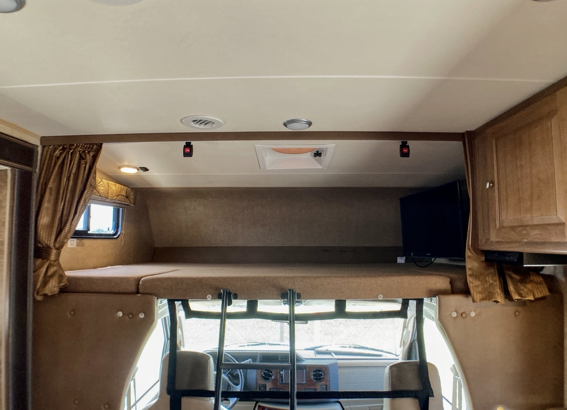 RV rental interior featuring the over-cab bed, a small TV, and ladder for comfortable travel.. Coachman Leprechaun 260DS 2017