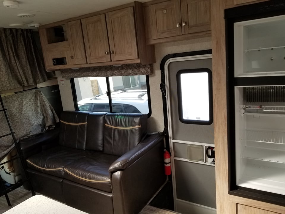 RV rental interior with a brown sofa, wood cabinets, and open fridge. A visible entry door & fire extinguisher. Ideal for travel.. Forester Forester Motorhome 2019