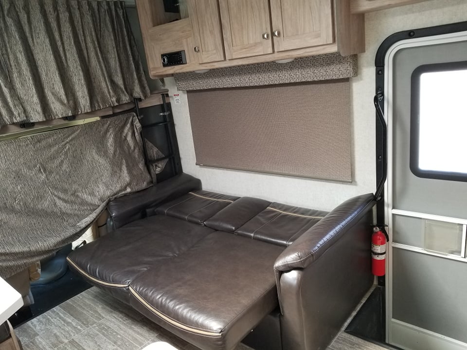 An RV rental interior showing a dark brown sofa bed, bunk area with privacy curtains, and compact living space.. Forester Forester Motorhome 2019