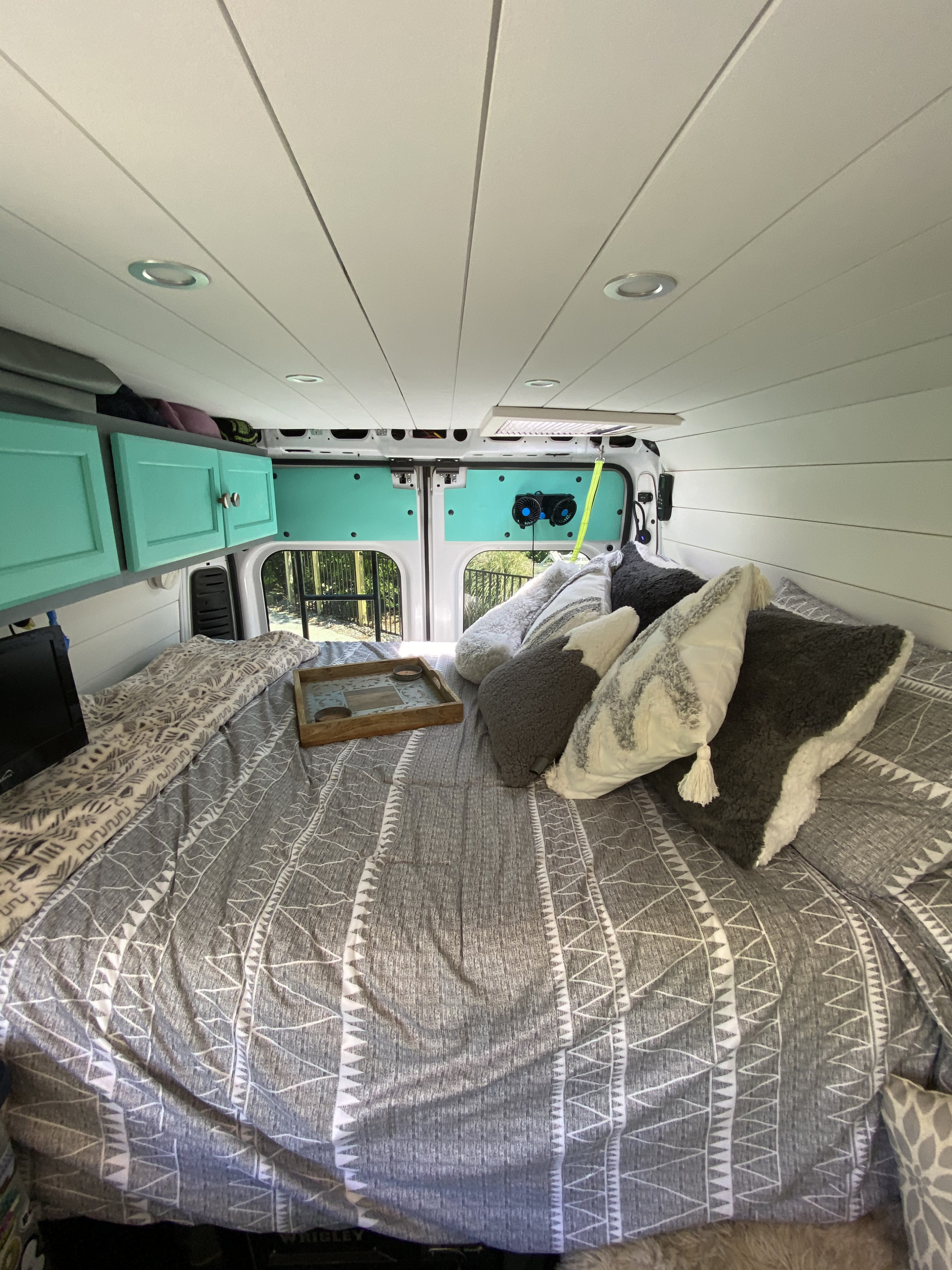 Cozy RV rental interior with bed, teal cabinets, and outdoor view. Perfect for mobile adventures.. Ram Promaster 2500 2018