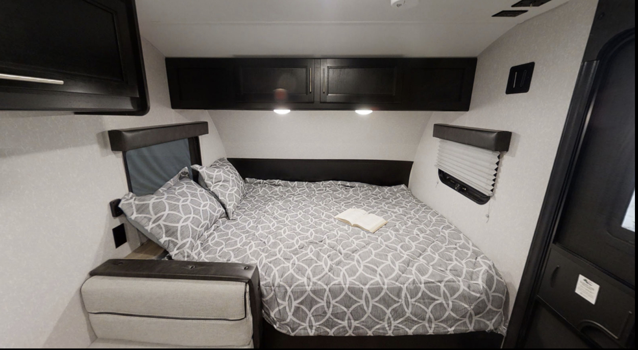 RV rental bedroom with comfortable bed, patterned bedding, overhead cabinets, and side windows. Perfect for travel.. Forest River Cherokee Wolf Pup Black Label 2022