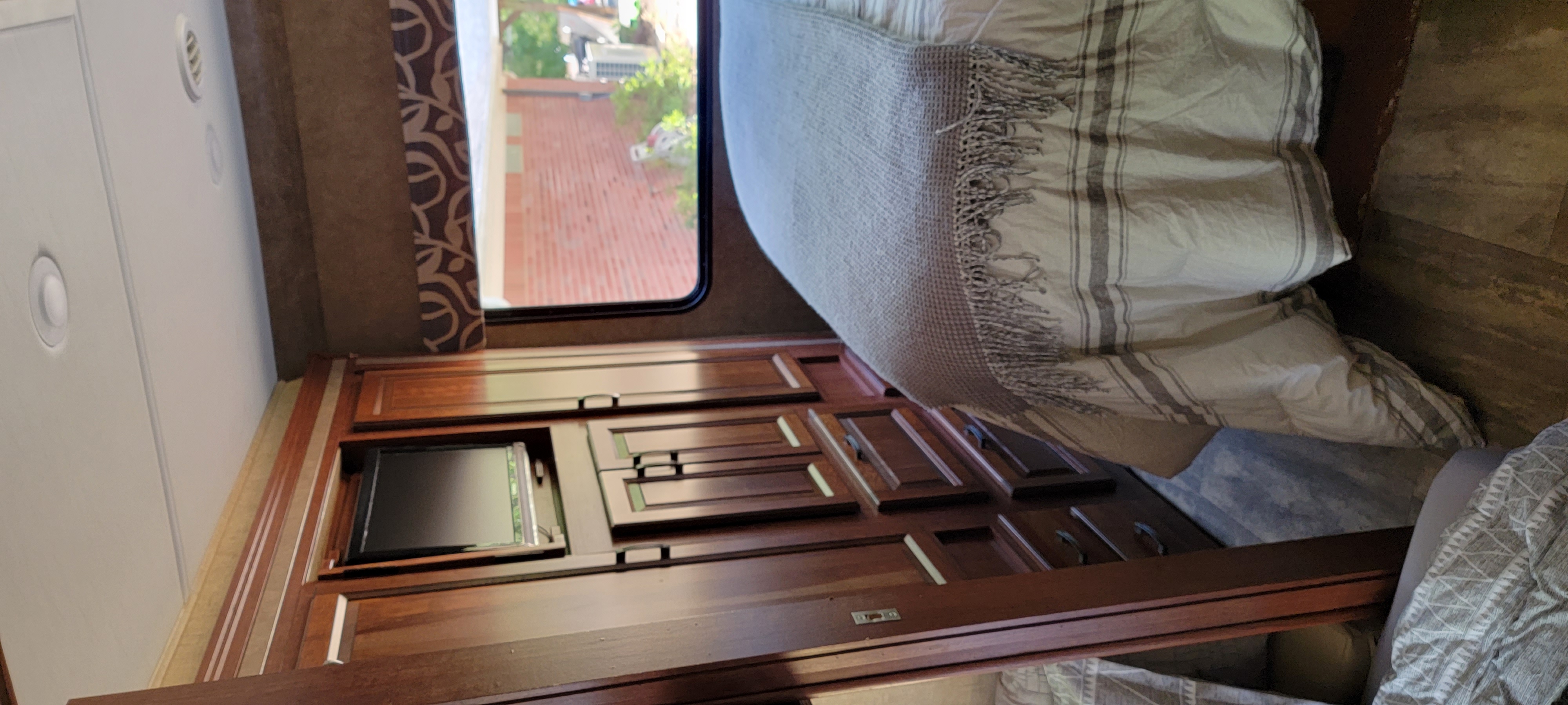 Inside a cozy RV rental bedroom featuring a bed, mounted TV, and wooden storage.. Forest River 3171DS 2016