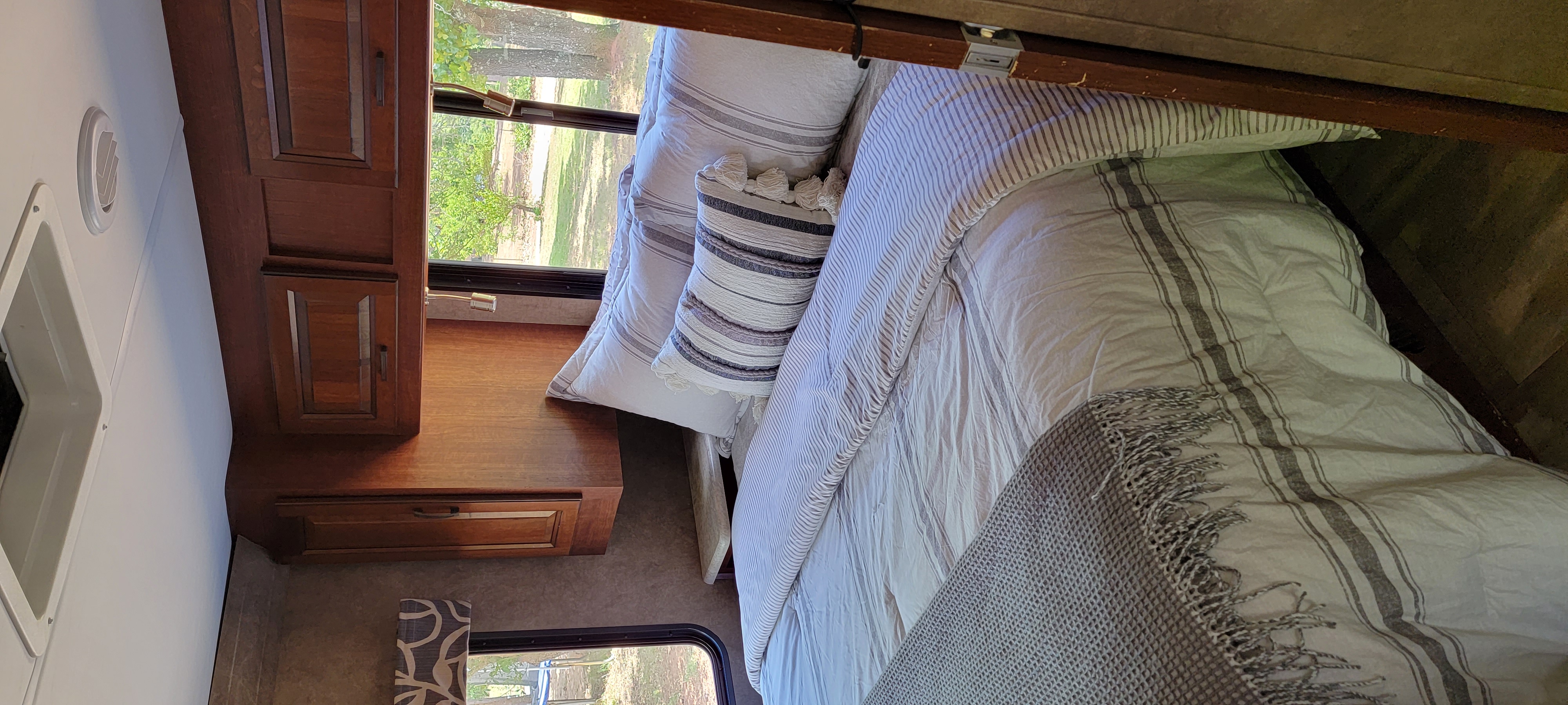 Interior of a comfortable RV rental bedroom, featuring striped bedding, wooden cabinets, and a scenic window view.. Forest River 3171DS 2016