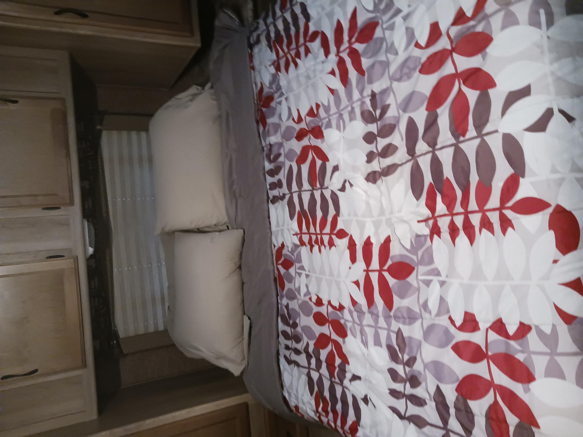 Inside this RV rental, a compact bedroom features a bed with a red and purple leaf-patterned comforter, pillows, and wood cabinets.. Coachmen Freelander 2014