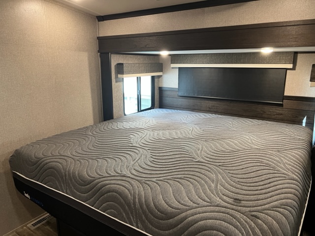Spacious RV rental bedroom with a large, grey textured mattress, dark wood headboard, and light walls. Perfect for travel.. Jayco North Point 2021