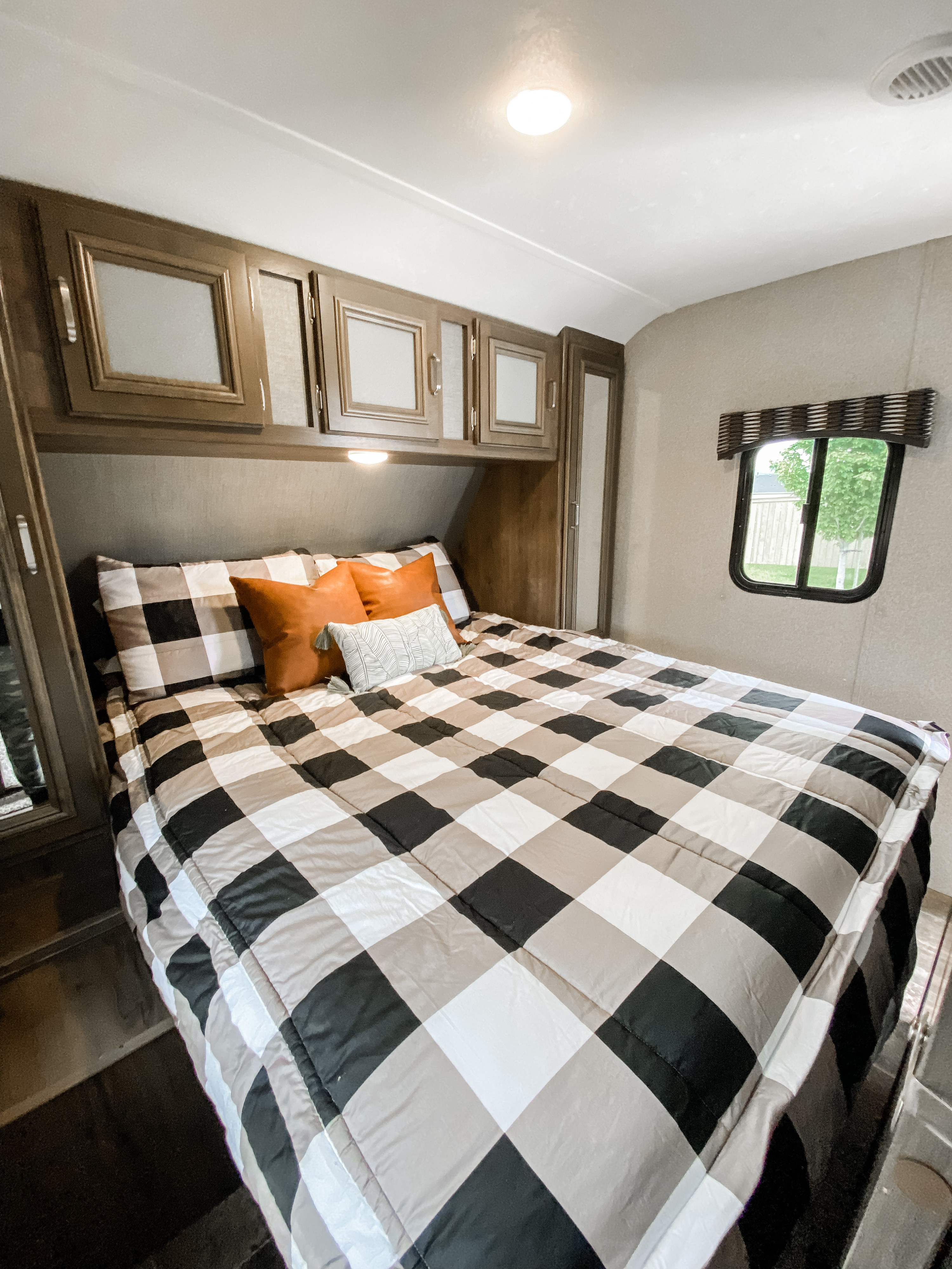 RV rental bedroom with a comfy black & tan buffalo check bed, overhead cabinets, & small window. Ideal for trips.. Keystone RV Passport Ultra Lite 2018
