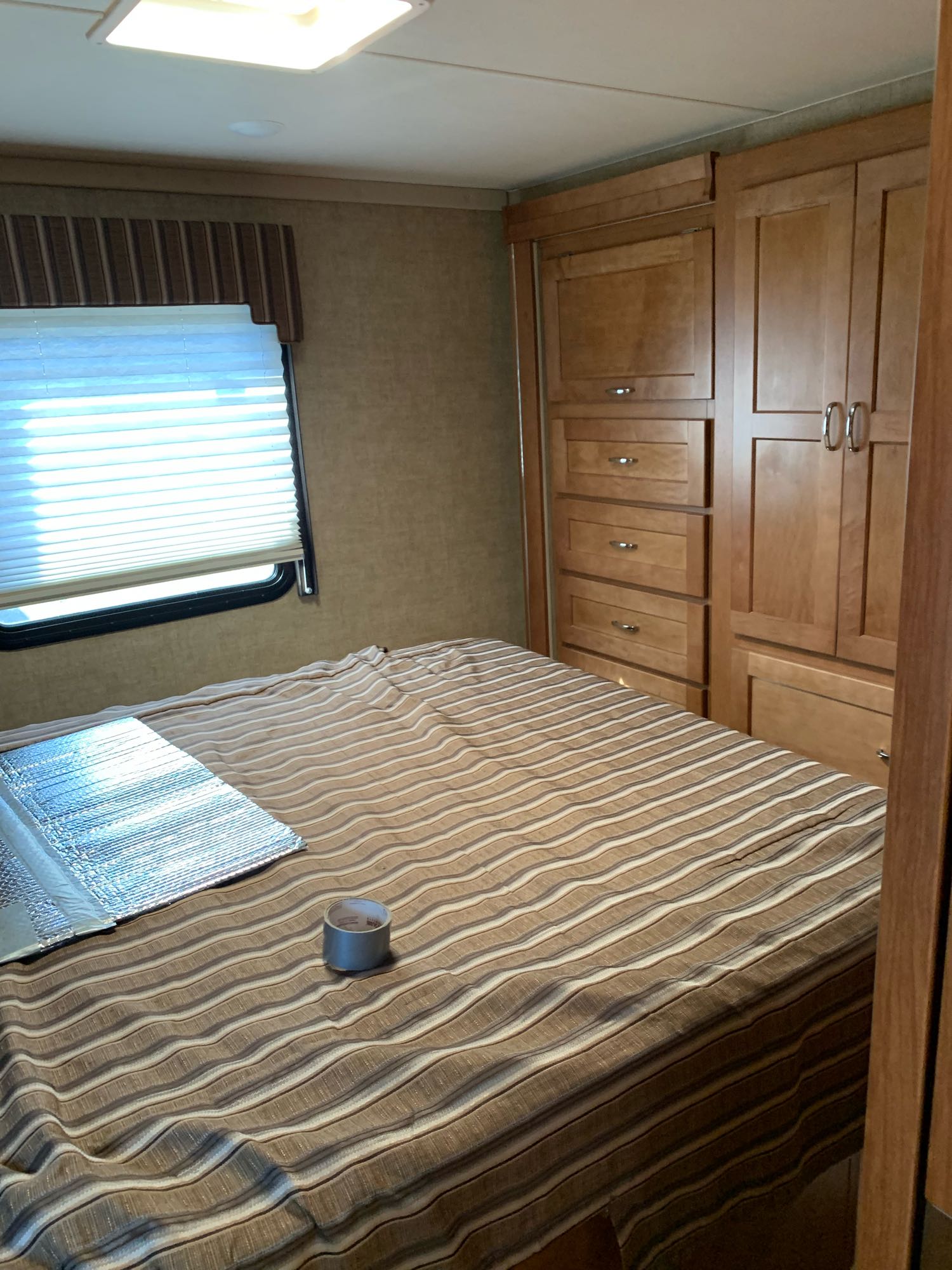 RV rental bedroom with bed, window, and wood storage. Reflective insulation & duct tape on bed provide context.. Winnebago Minnie Winnie 2018