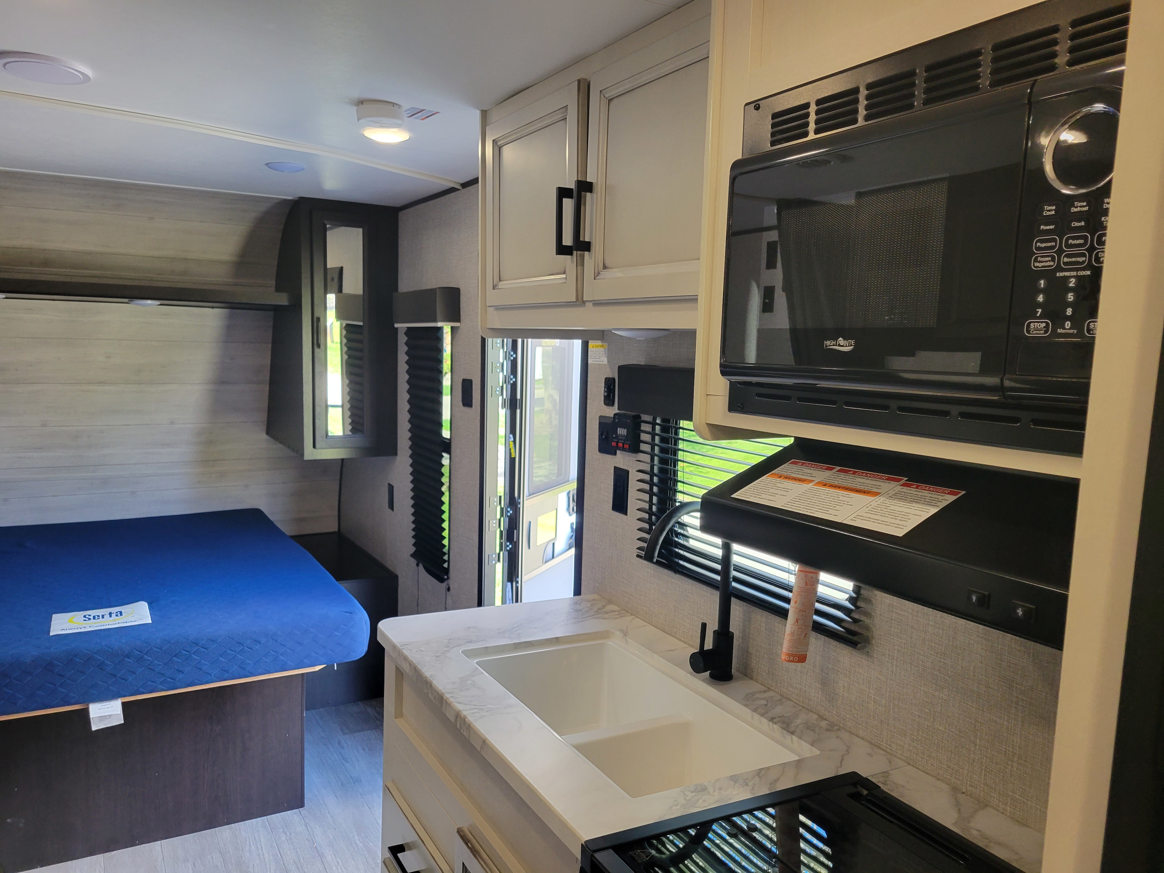 Compact RV rental interior featuring a functional kitchen with a microwave, sink, and stove, adjacent to a cozy bedroom area with a bed.. Jayco Jay Flight SLX 2022
