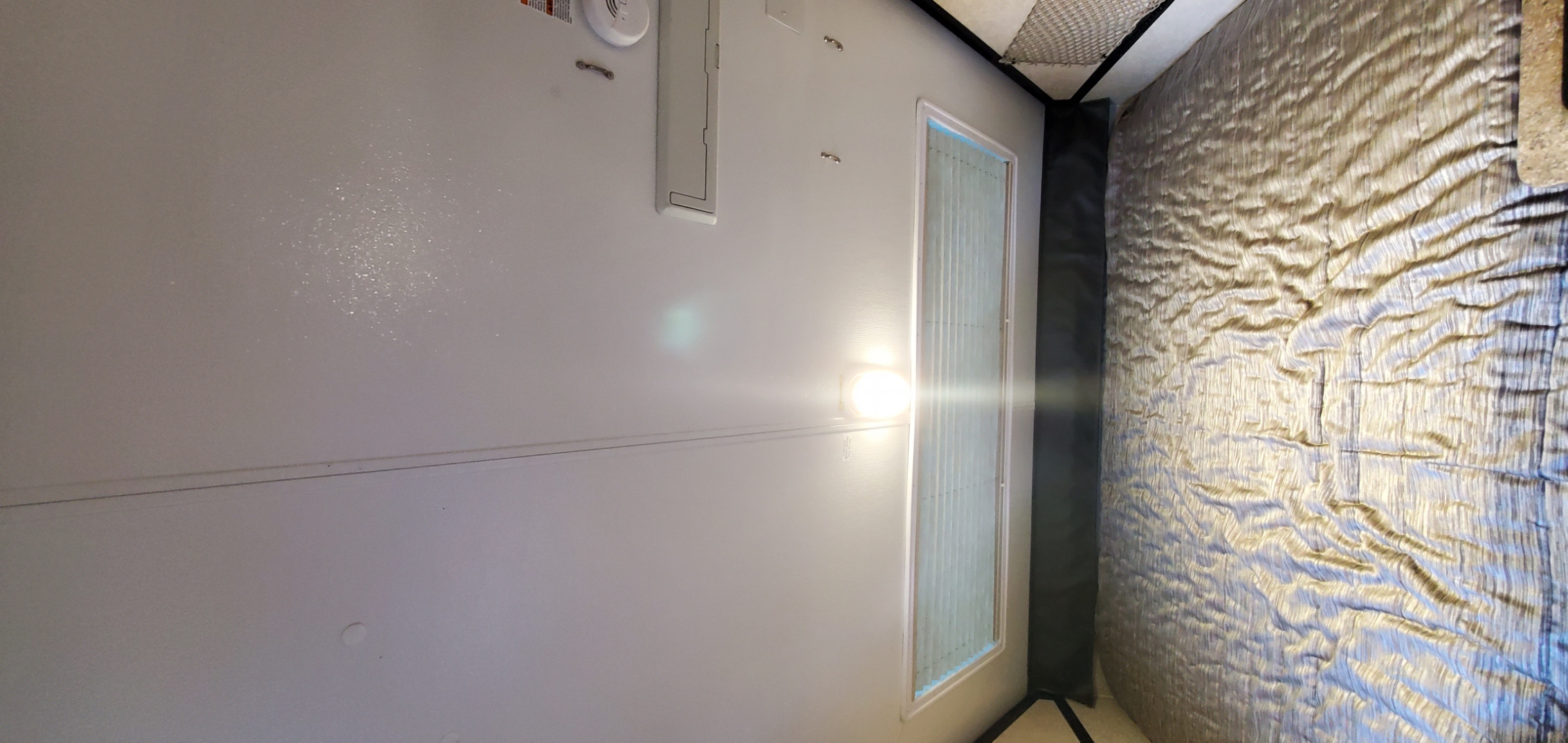 RV rental interior: bright wall light illuminating a textured, wrinkled bed and window in a compact space.. Forest River Rockwood Premier 2018