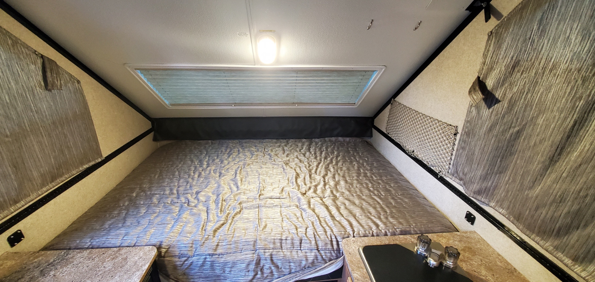 Cozy RV rental interior featuring a spacious bed, overhead skylight, and a small countertop. Ideal for camping.. Forest River Rockwood Premier 2018
